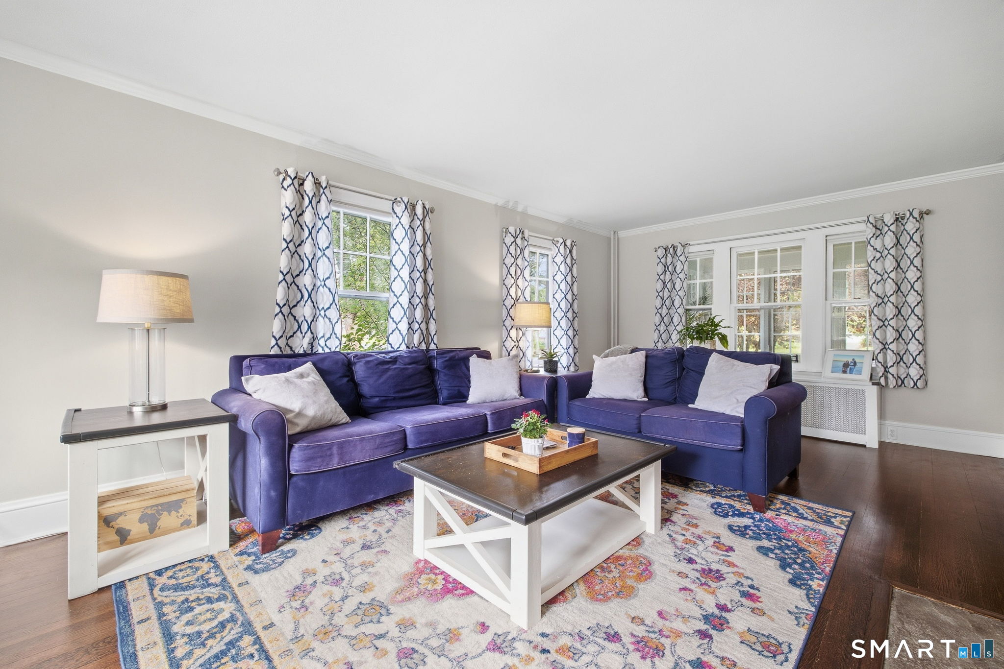 Living room with blue sofas, large windows, patterned curtains, and a colorful floral rug.