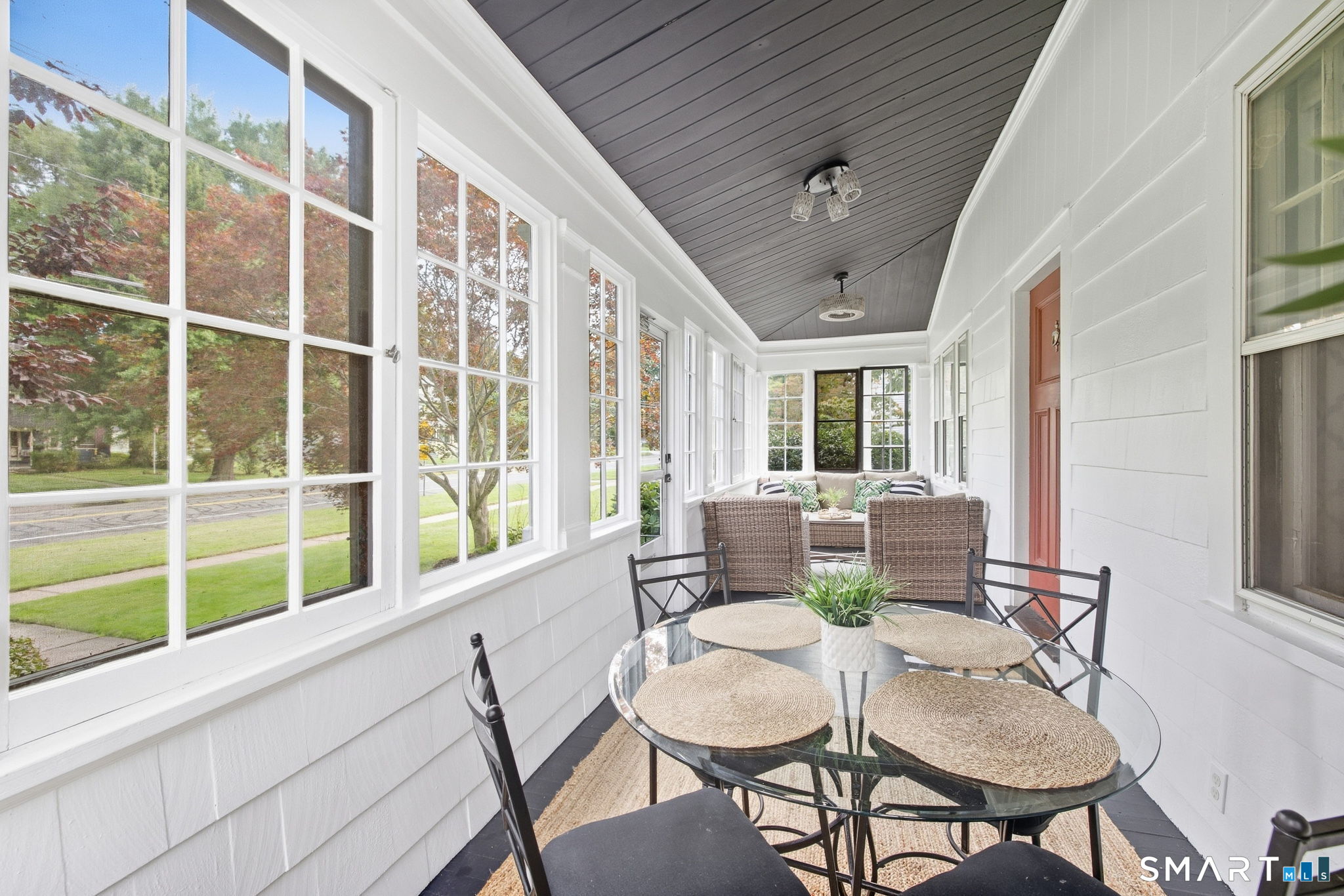 Enclosed sunroom with large windows, a glass dining table, and wicker seating.