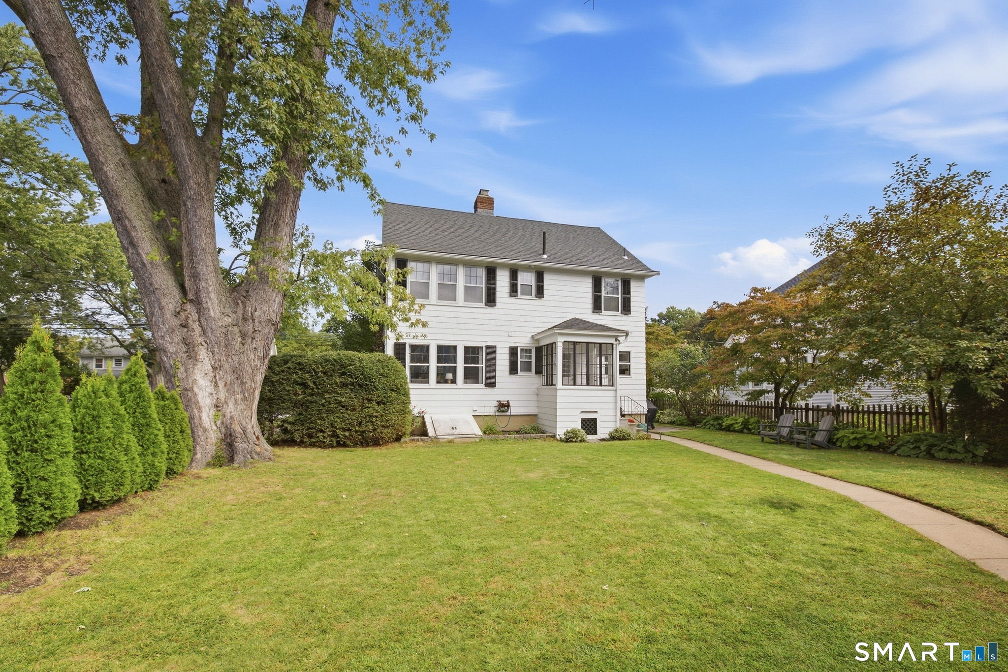 White two-story house with a screened porch, mature shade tree, and spacious lawn.