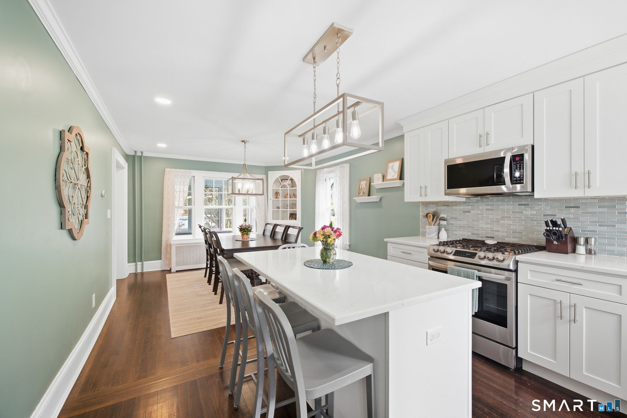 Kitchen with a large white island, stainless steel range, and dining table beside curtained windows.