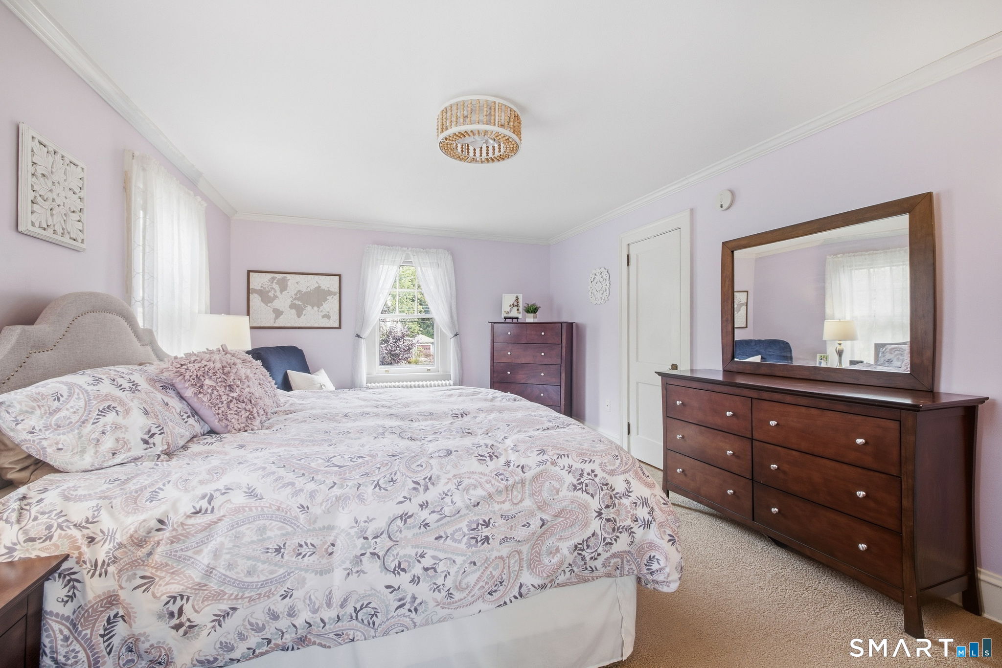 Furnished bedroom with lavender walls, a patterned bedspread, and dark wood dressers.