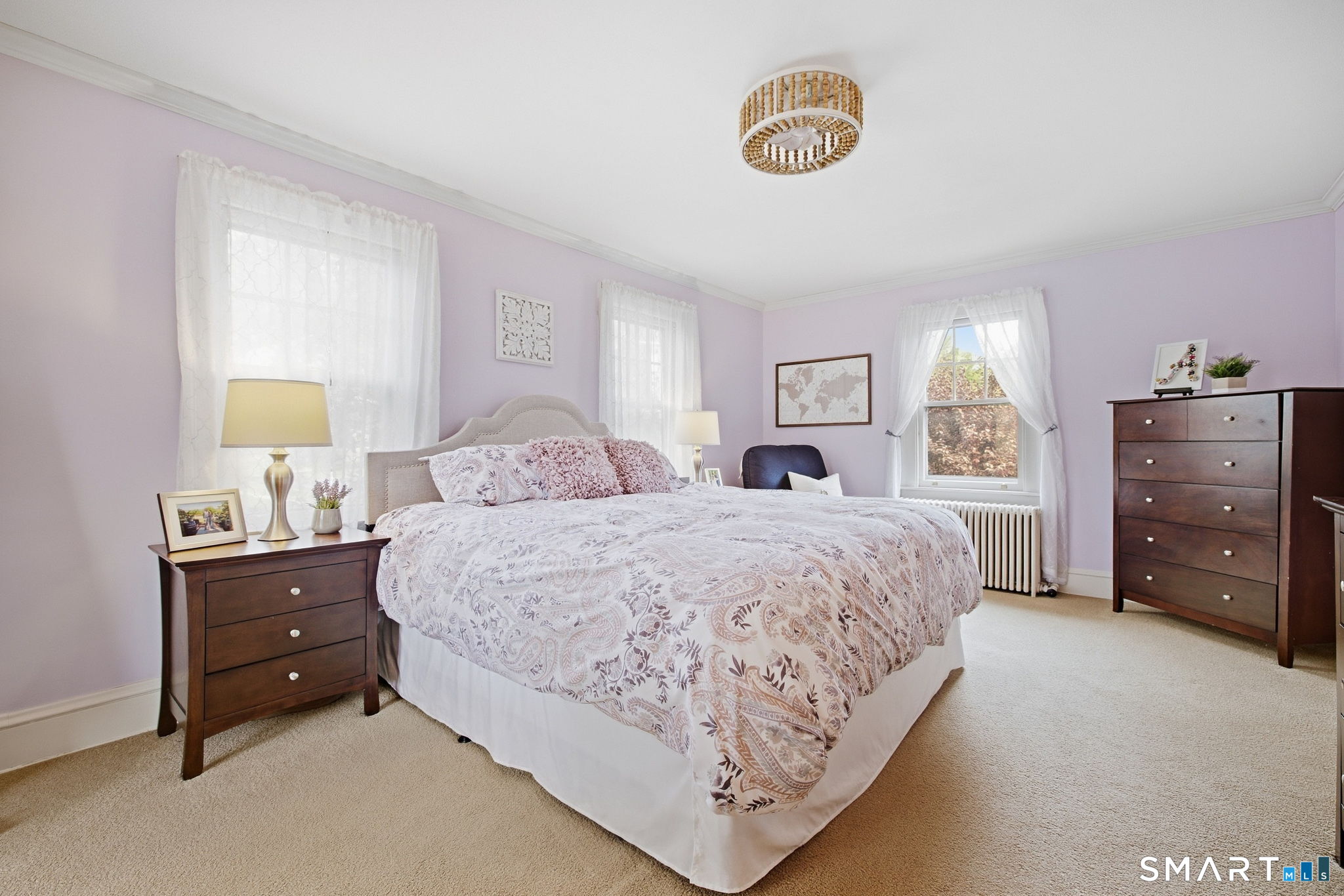 Bedroom with a patterned bed, lavender walls, sheer curtains, and dark wood dressers.