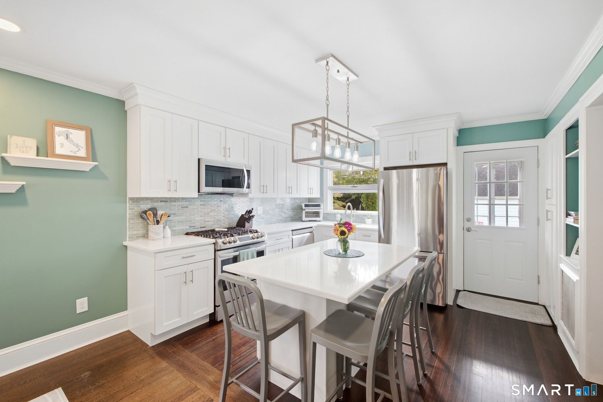 Bright kitchen with a large white island, stainless steel appliances, and green walls.