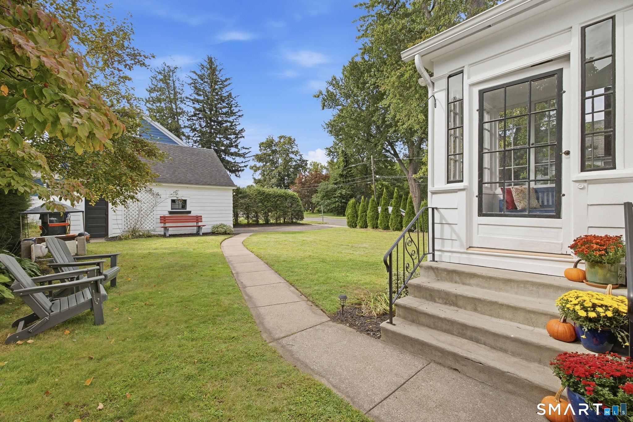 White house entrance with concrete steps, a curved walkway, lawn, outdoor chairs, and a detached shed.