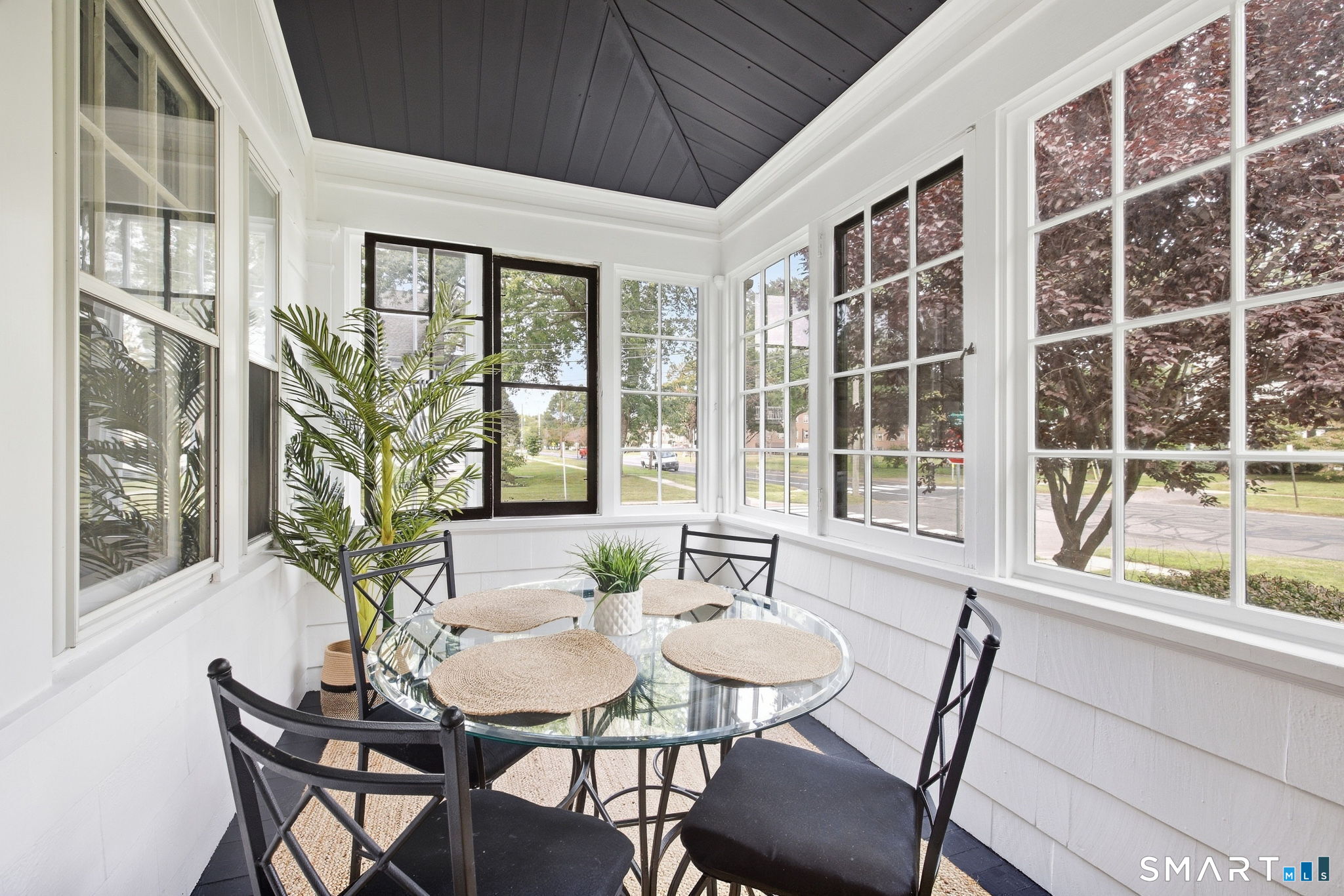Enclosed sunroom with a round glass dining table, black chairs, and large windows.