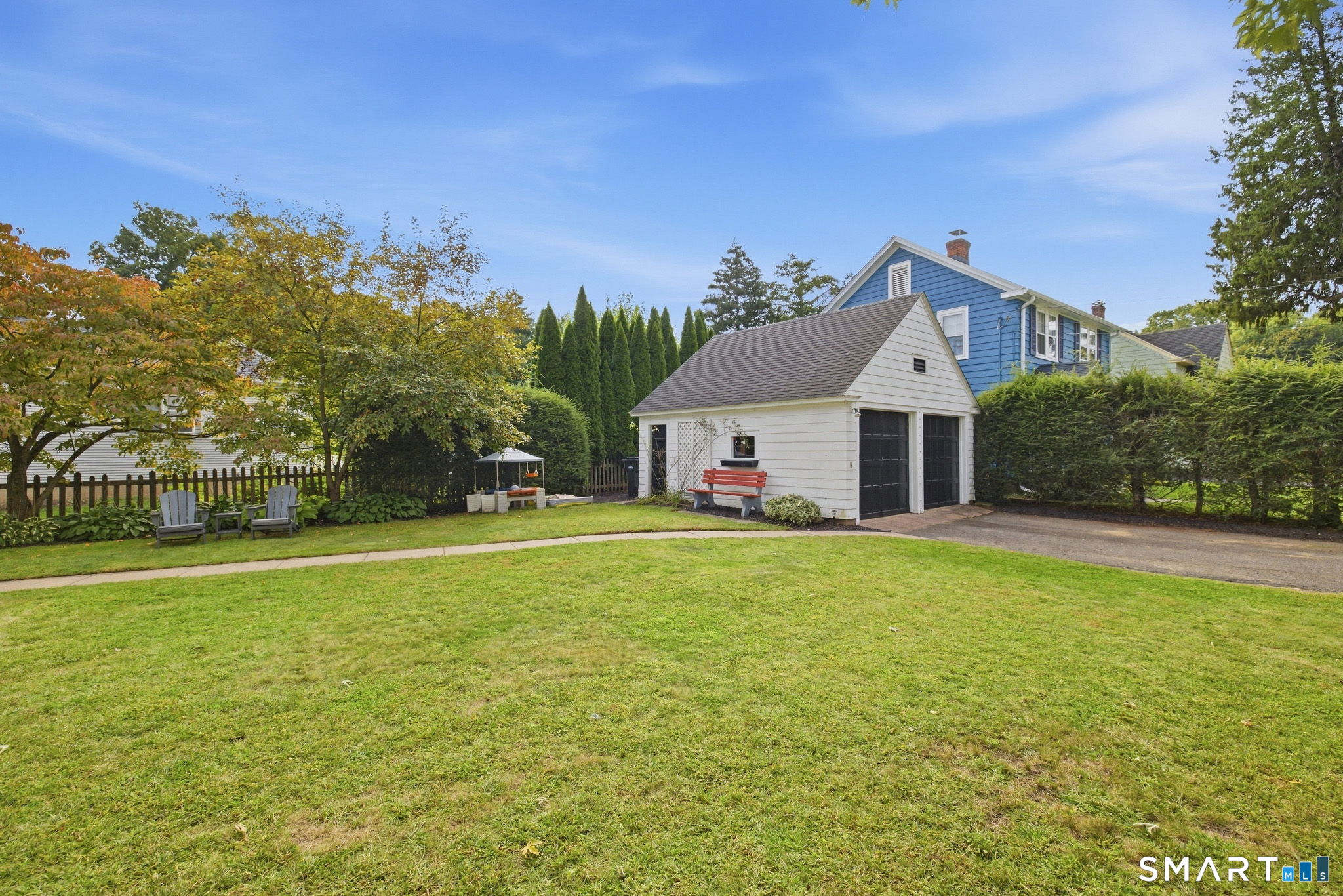 Backyard with a white detached garage, blue house, red bench, and leafy trees.
