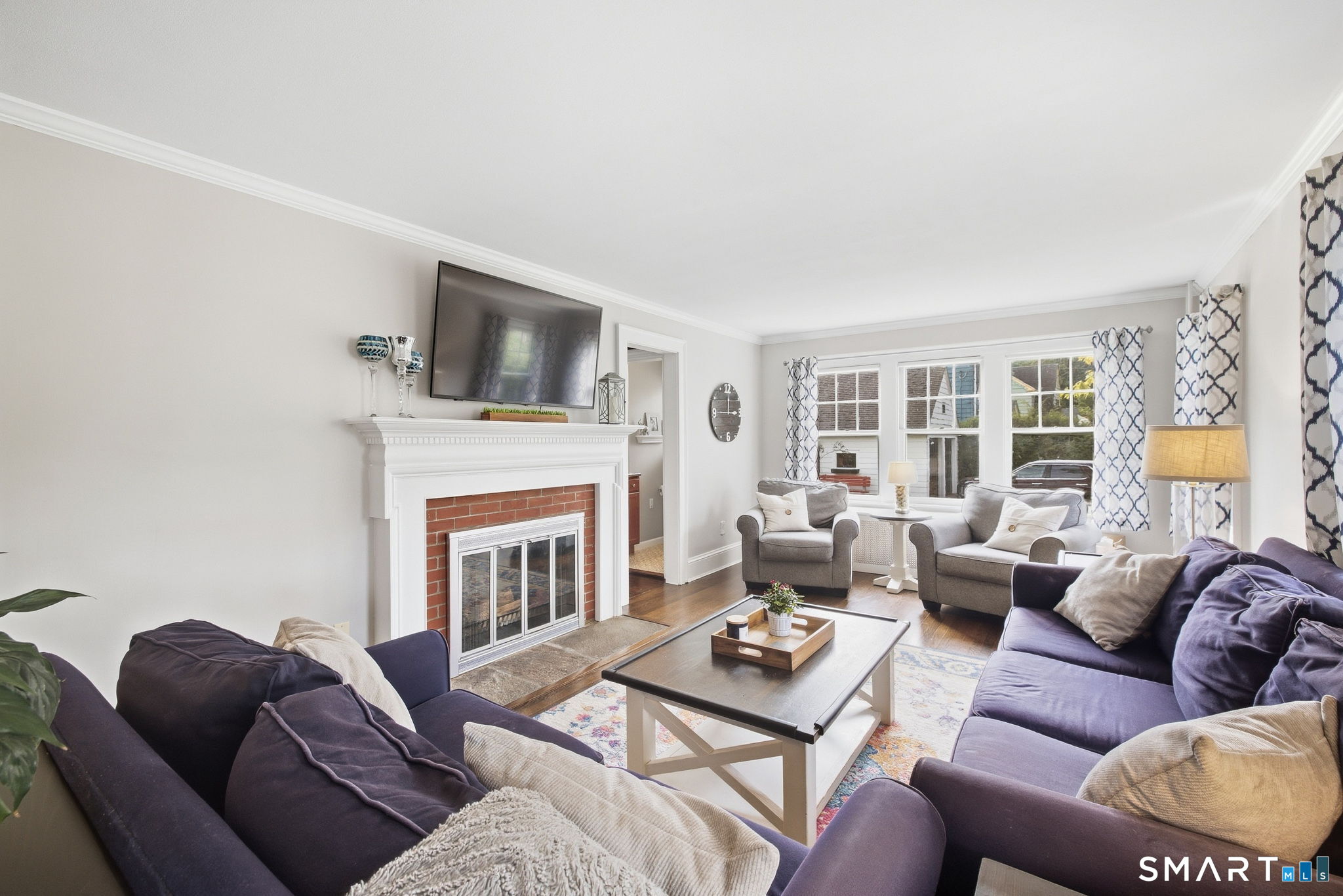 Furnished living room with a brick fireplace, purple sofas, and large windows.