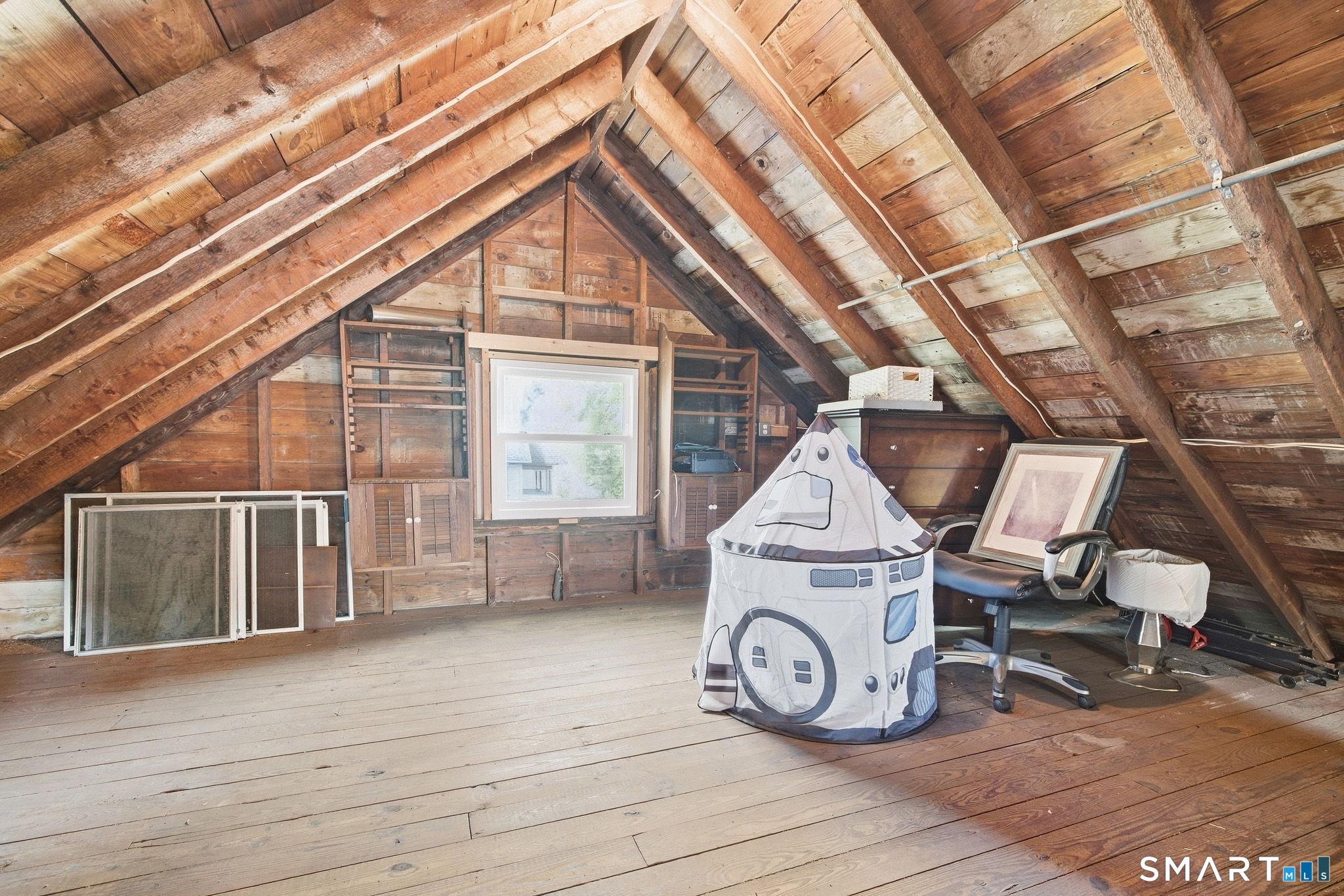 Wood-paneled attic with exposed rafters, built-in storage, and a child’s play tent.
