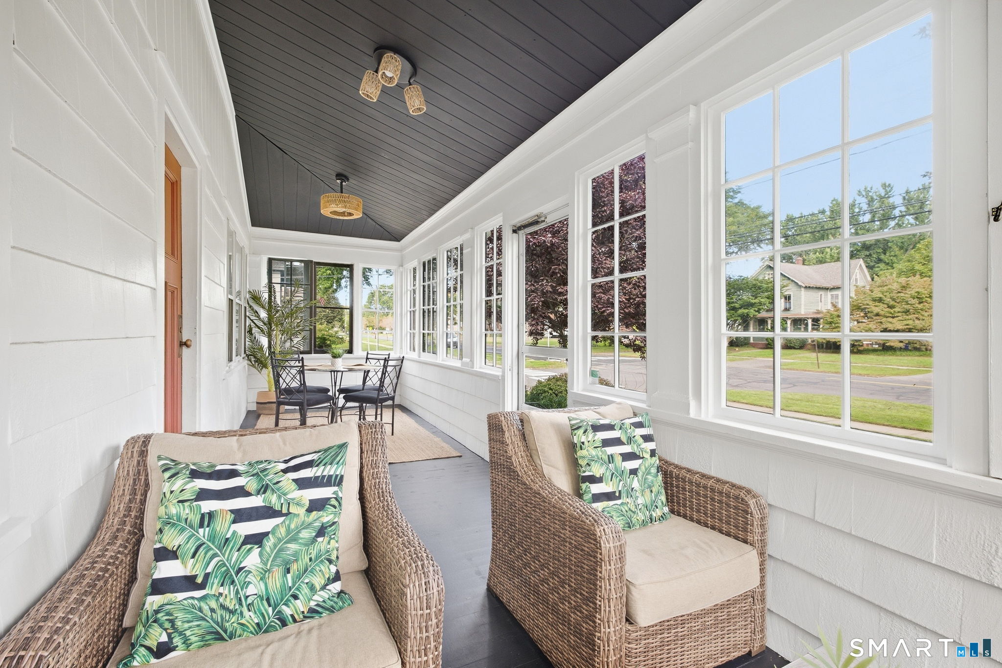 Enclosed porch with wicker armchairs, a dining set, and large windows overlooking the street.