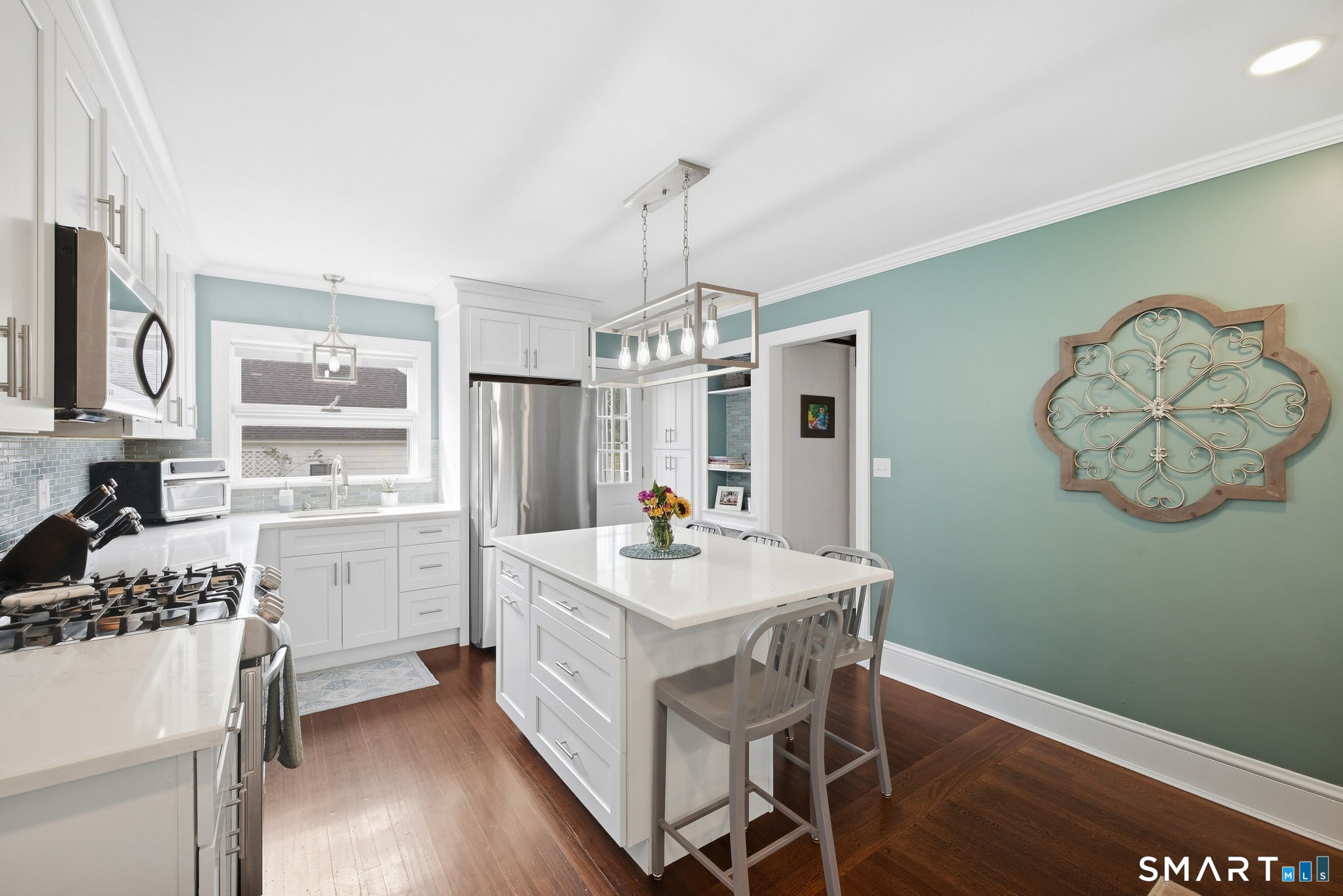 Bright kitchen with white cabinetry, stainless steel appliances, a large island, and dark hardwood floors.