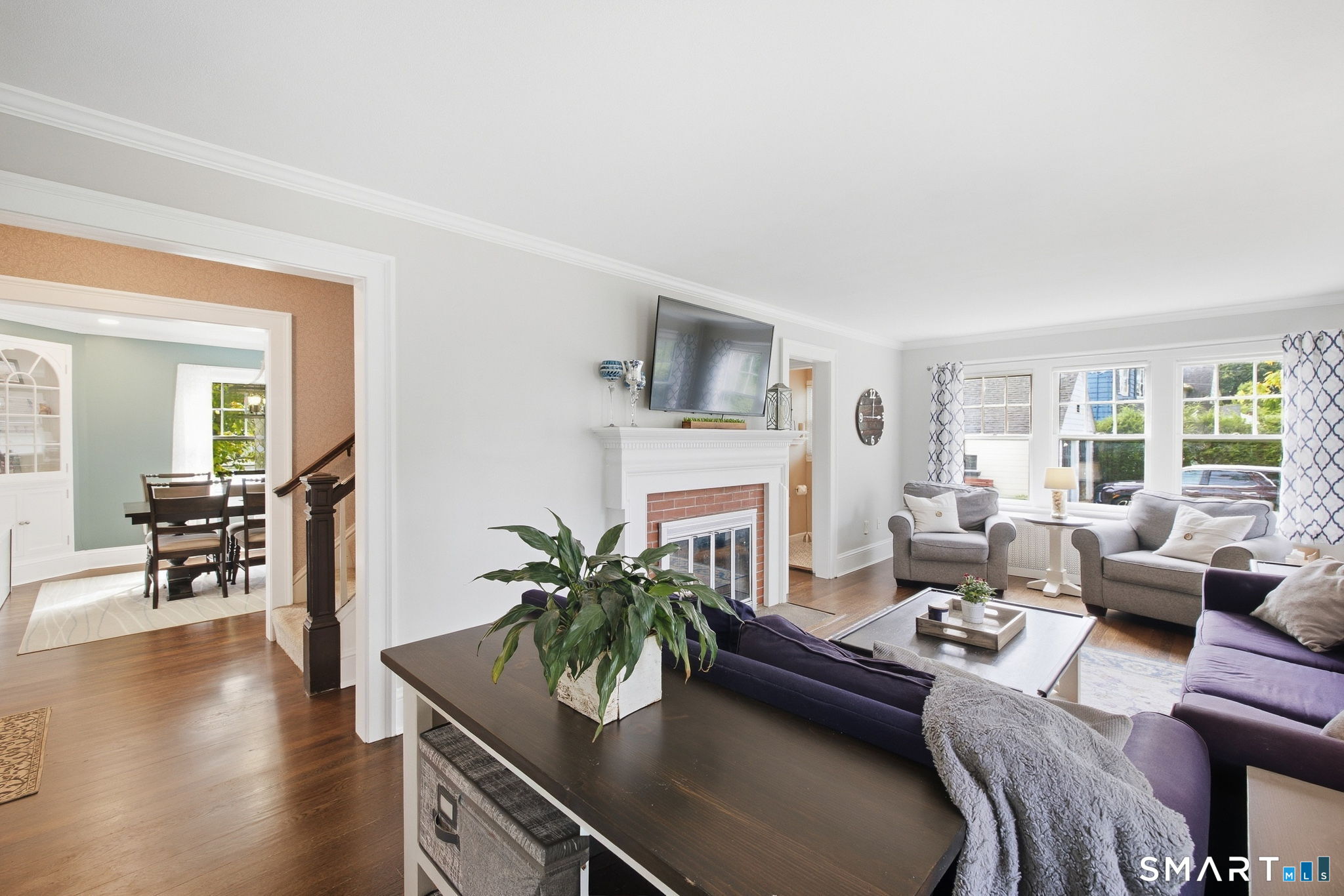 Living room with brick fireplace, gray seating, large windows, and an open doorway to the dining room.