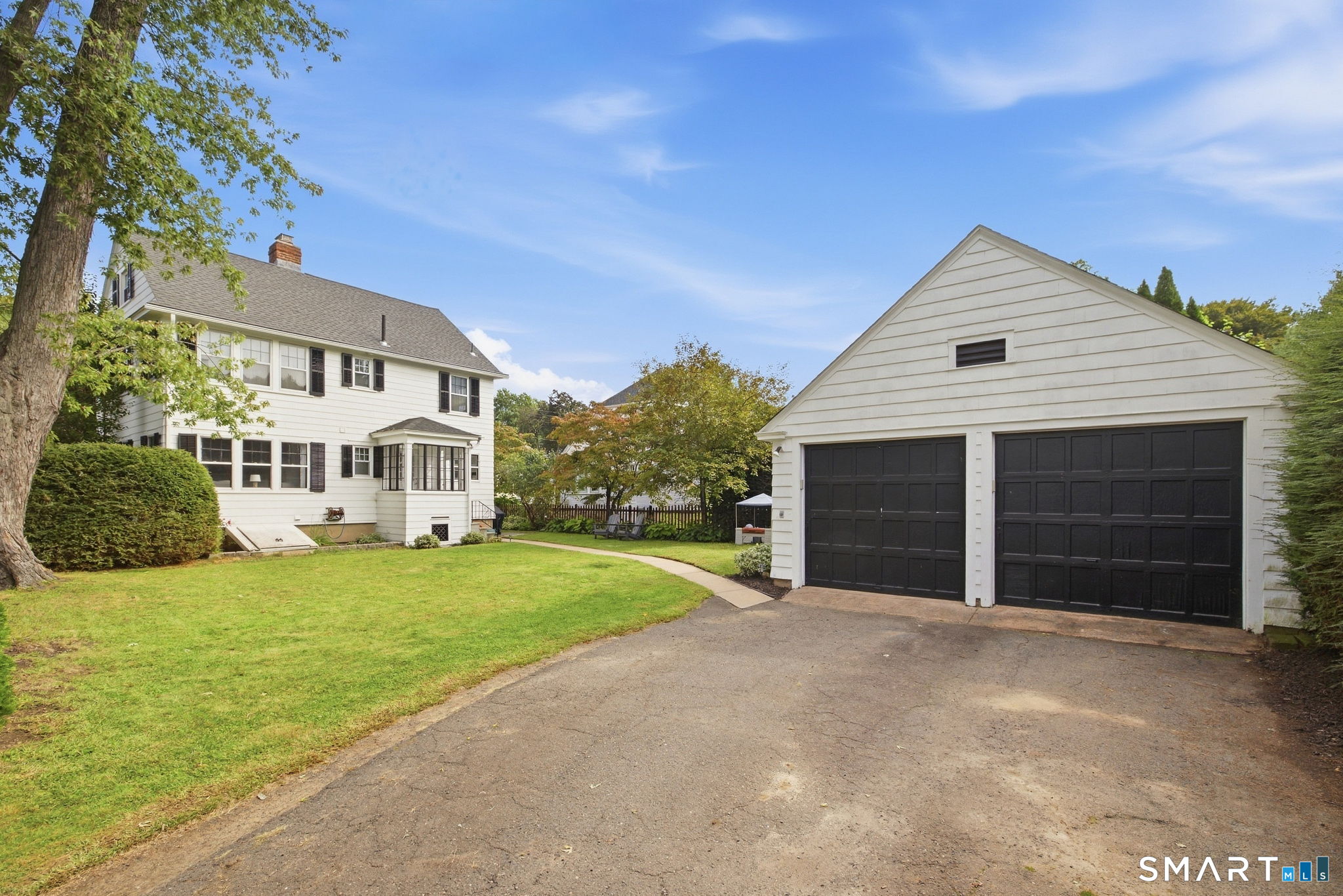 White two-story house beside a detached garage with two black doors and a paved driveway.