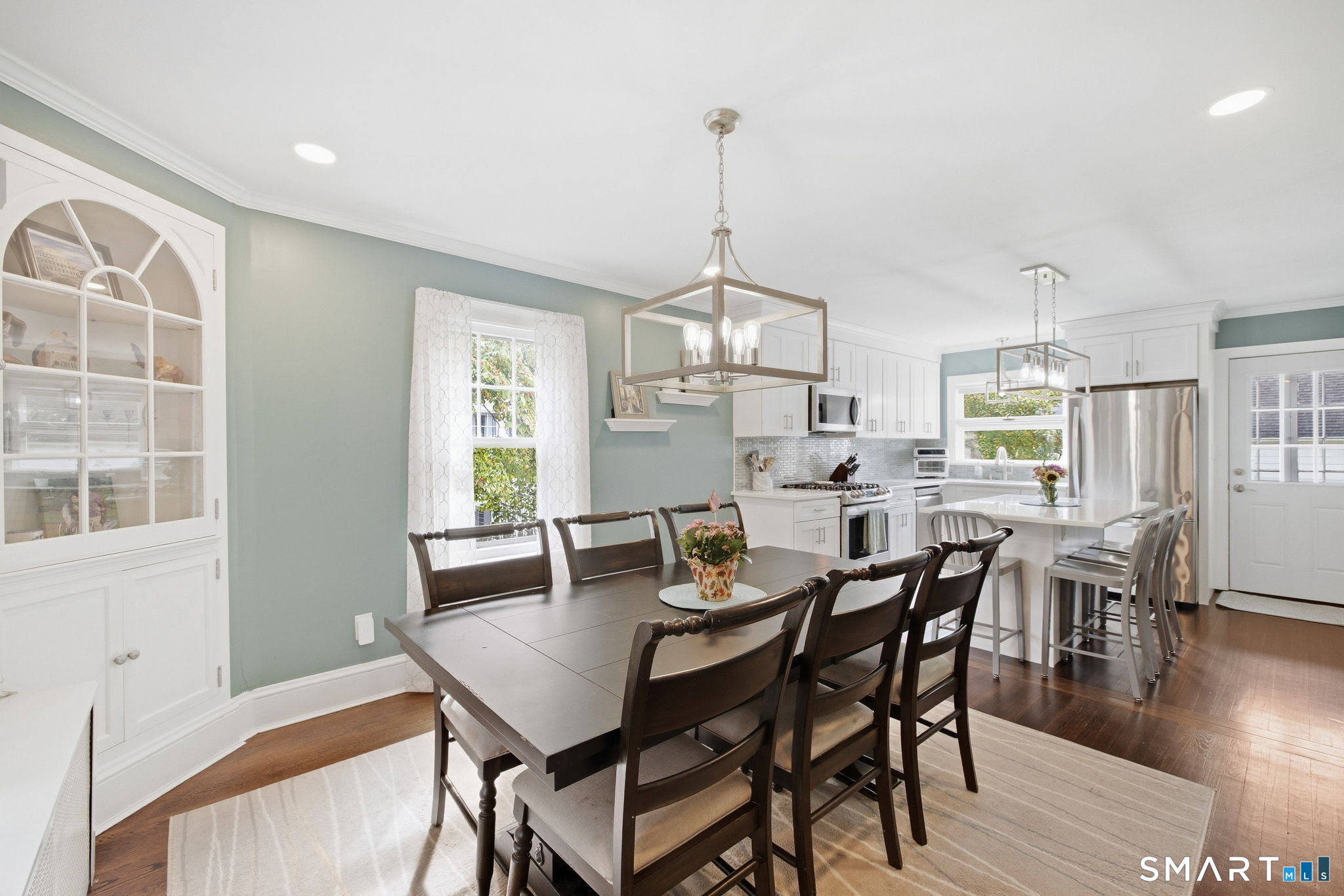 Furnished kitchen and dining area with white cabinetry, stainless steel appliances, and a large dark wood table.