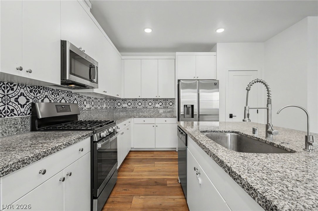 Modern kitchen with white cabinetry, granite counters, patterned tile backsplash, stainless steel appliances, and wood-look floors.