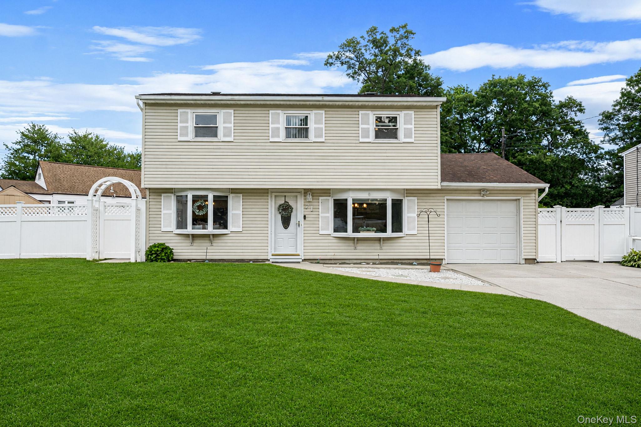 Two-story beige house with attached garage, broad lawn, and white fence with an arched gate.