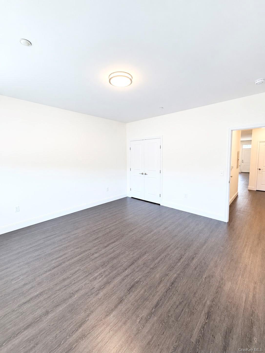 Empty room with gray wood-look flooring, double closet doors, and an open doorway to the hall.