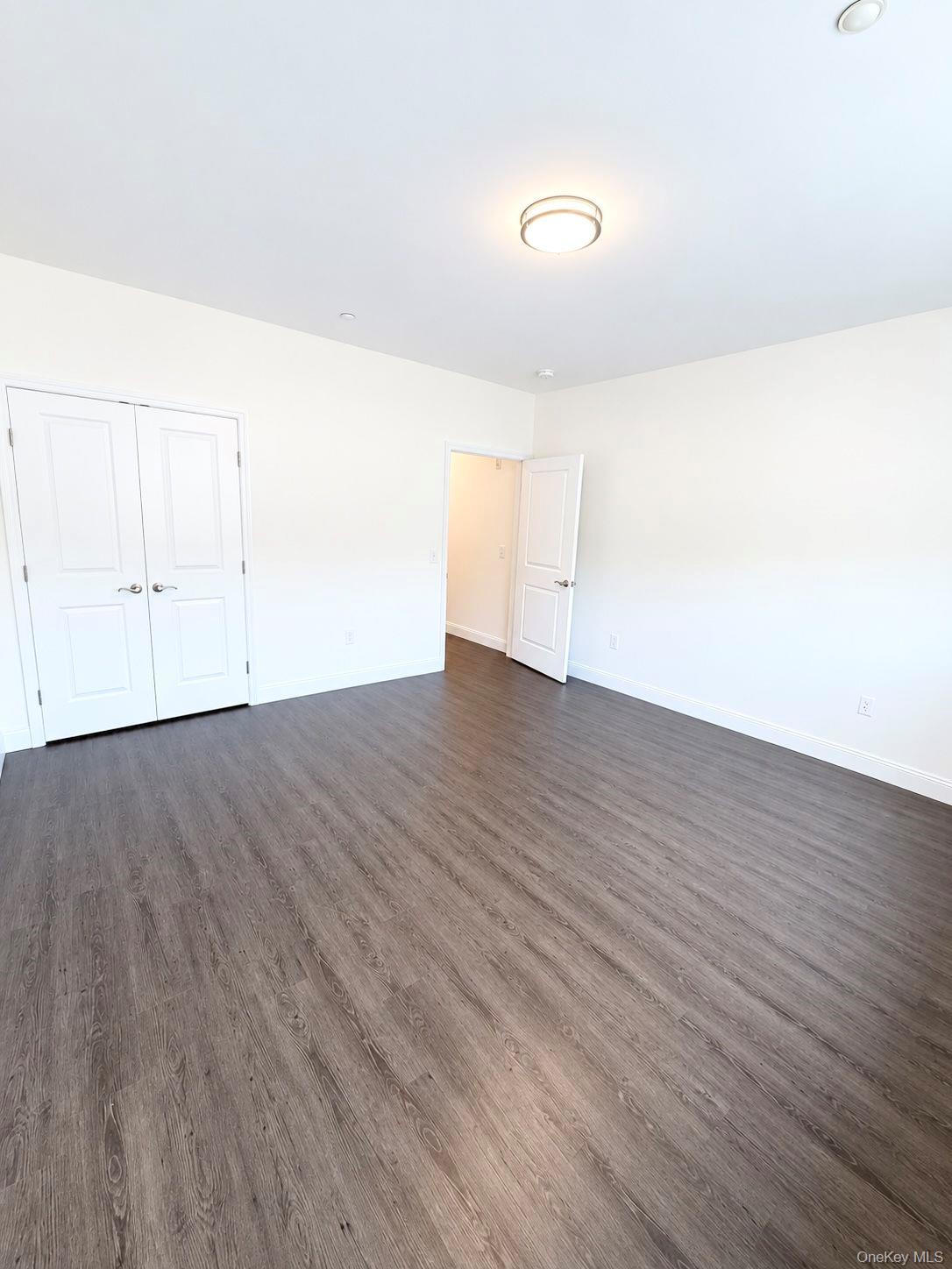 Empty room with gray-brown wood-look flooring, double closet doors, and an open doorway.