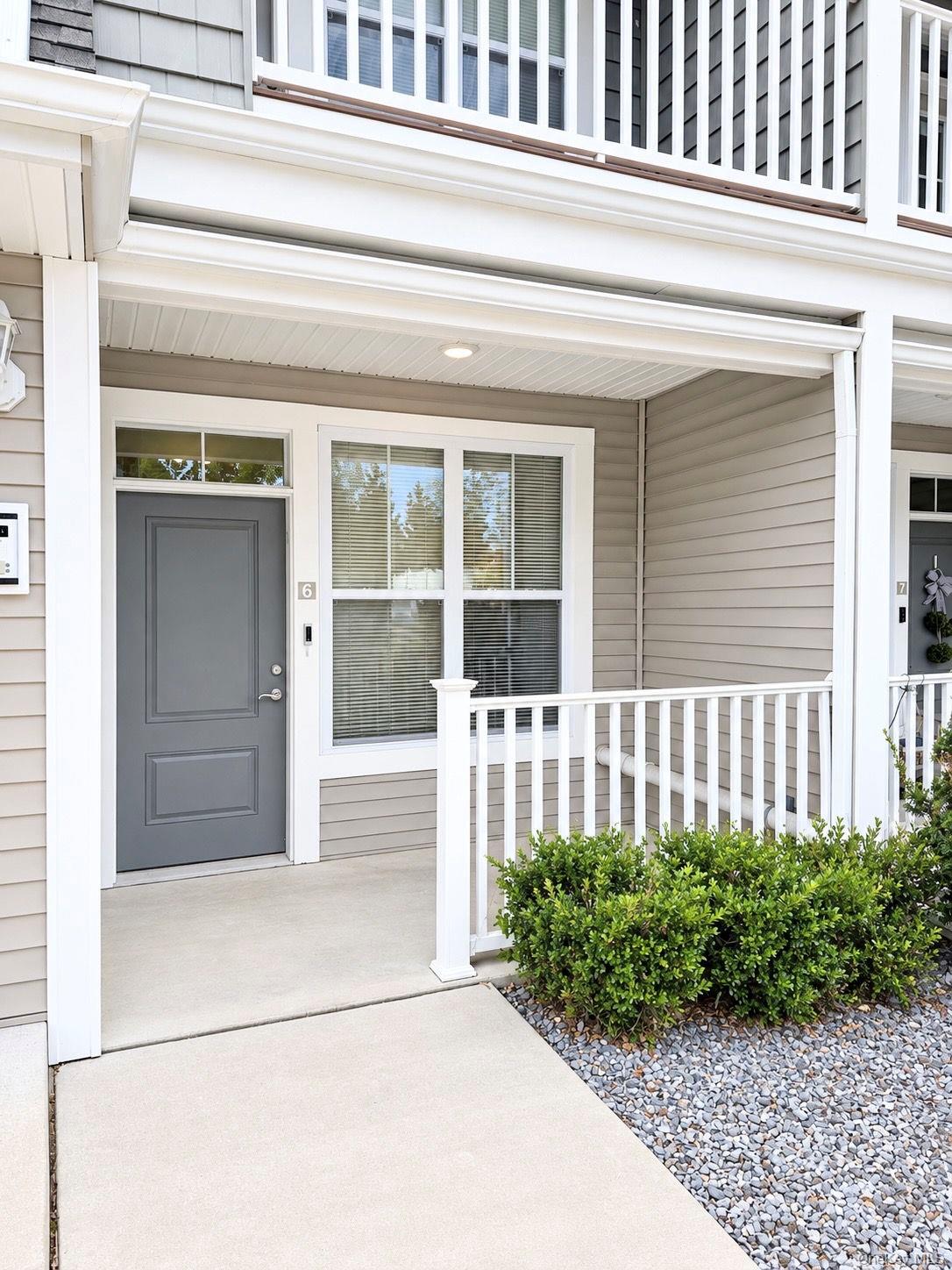 Unit 6 entrance with a gray door, covered porch, white railing, and large window.