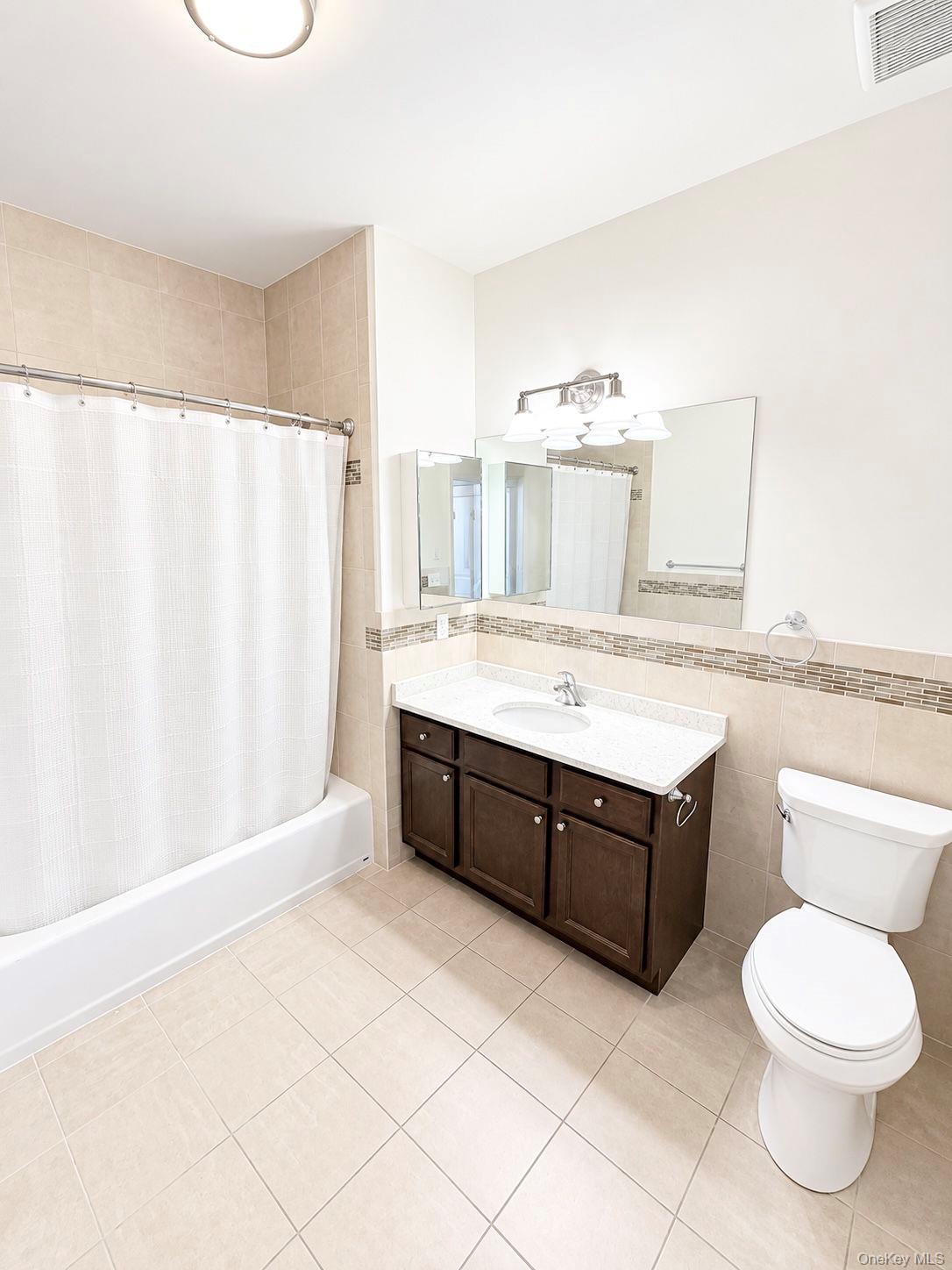 Bathroom with tiled tub and shower, dark wood vanity, large mirror, and white toilet.