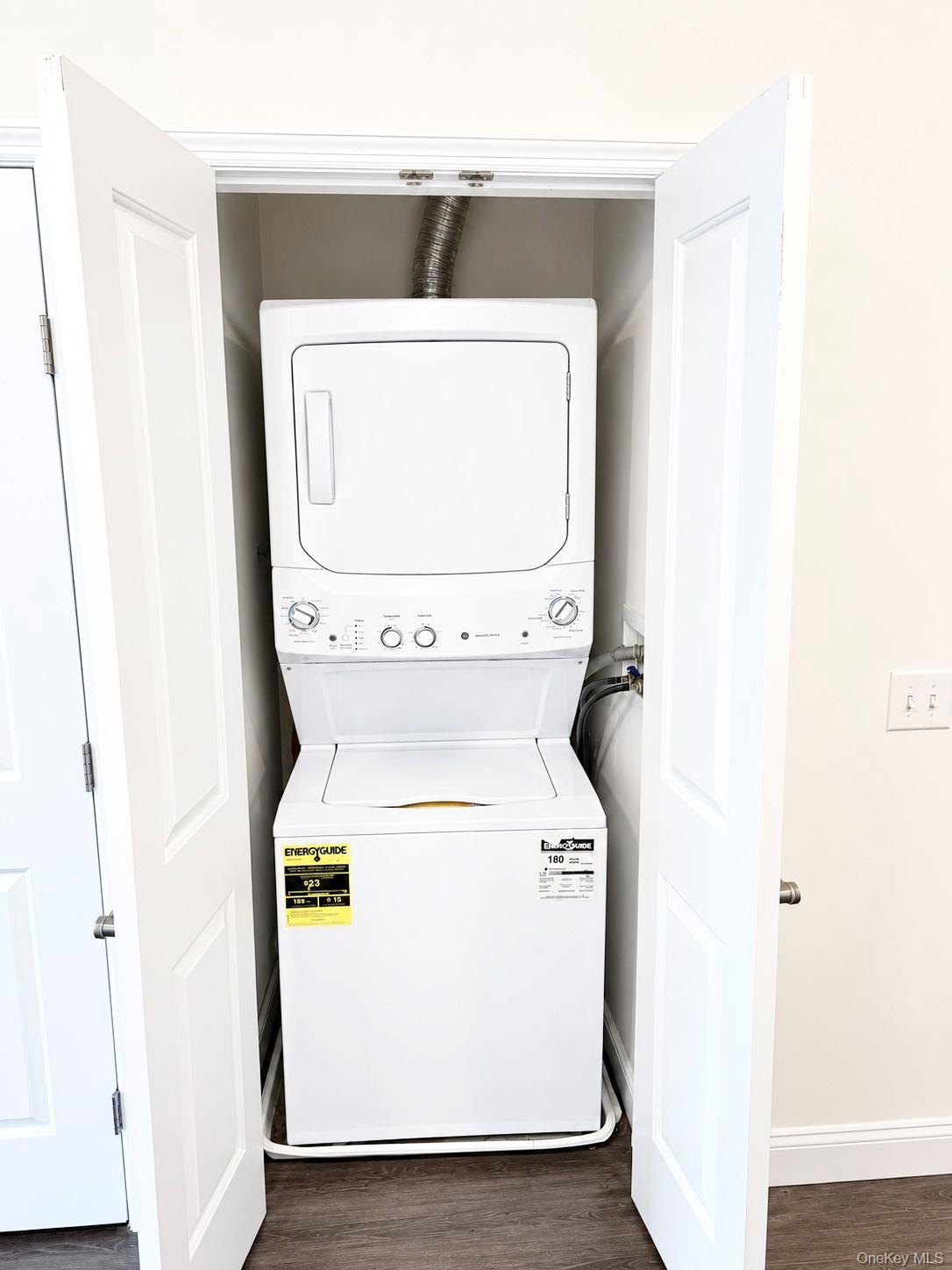 Stacked washer and dryer in a closet behind open white doors.