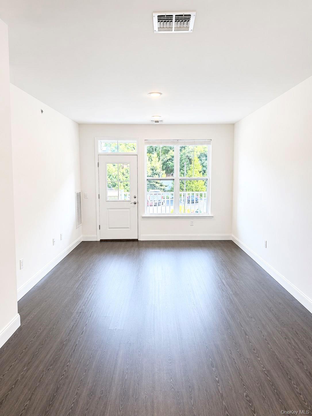 Empty room with dark plank flooring, a glass-paneled door, and a large window.