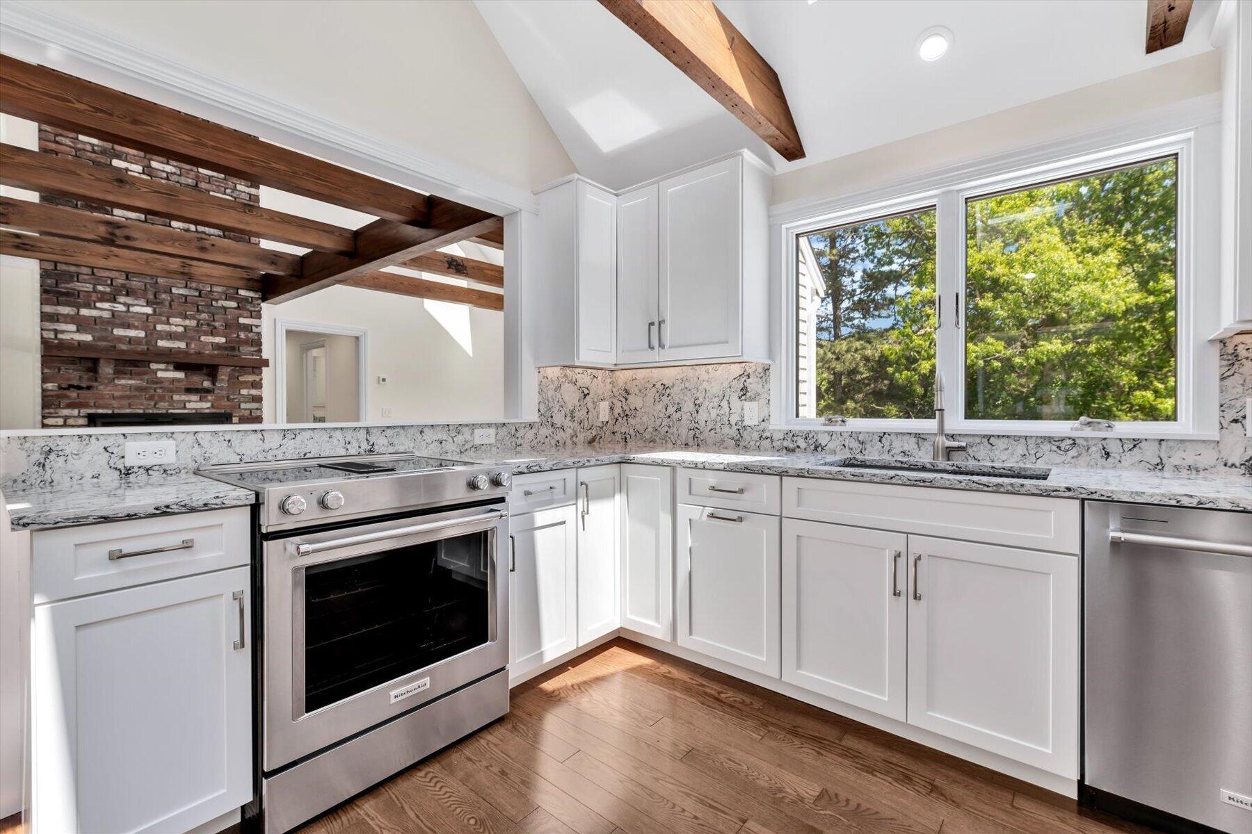 Bright kitchen with white cabinets, veined stone counters, stainless steel appliances, and exposed ceiling beams.