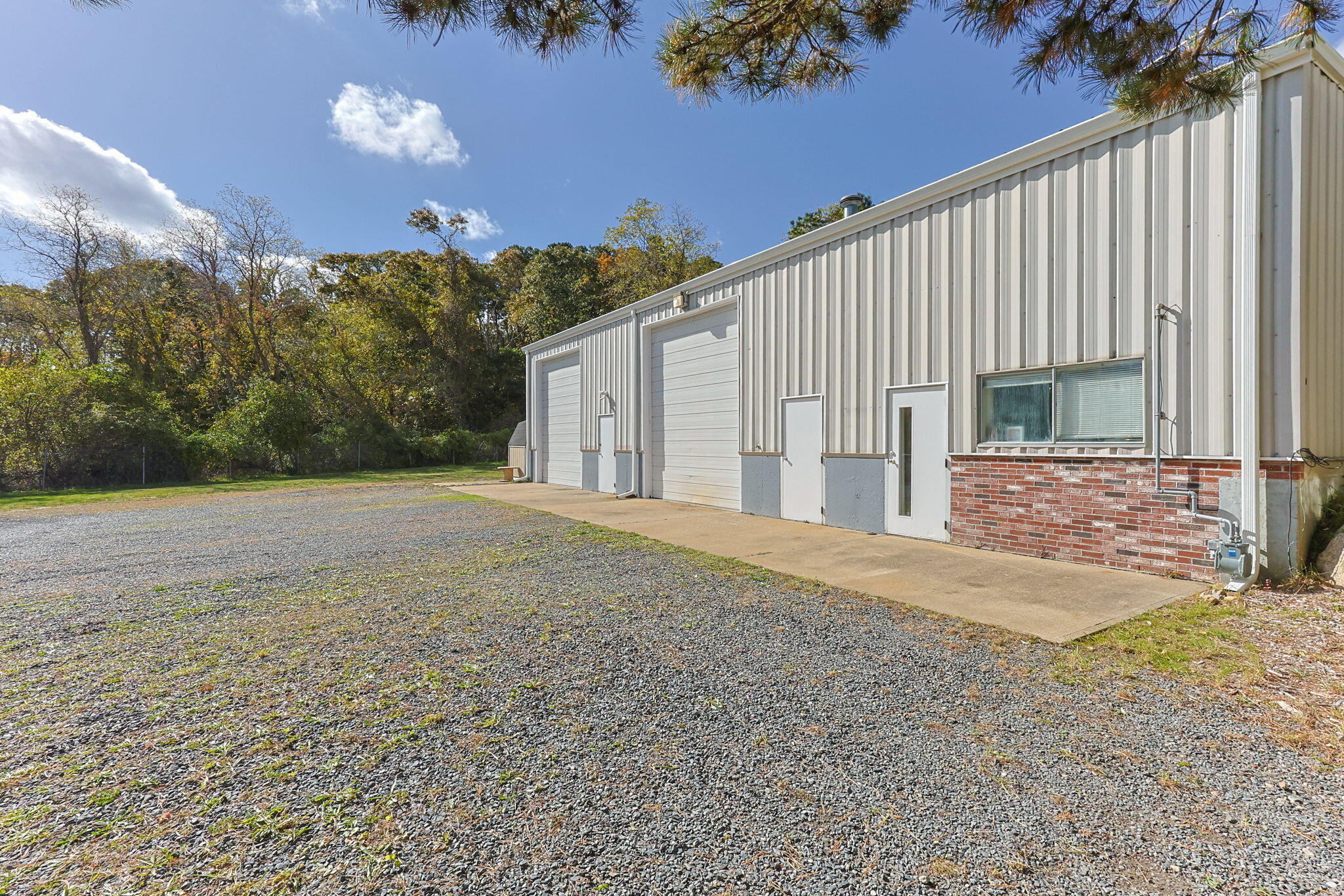 Commercial building with two large garage doors beside a broad gravel lot and wooded edge.