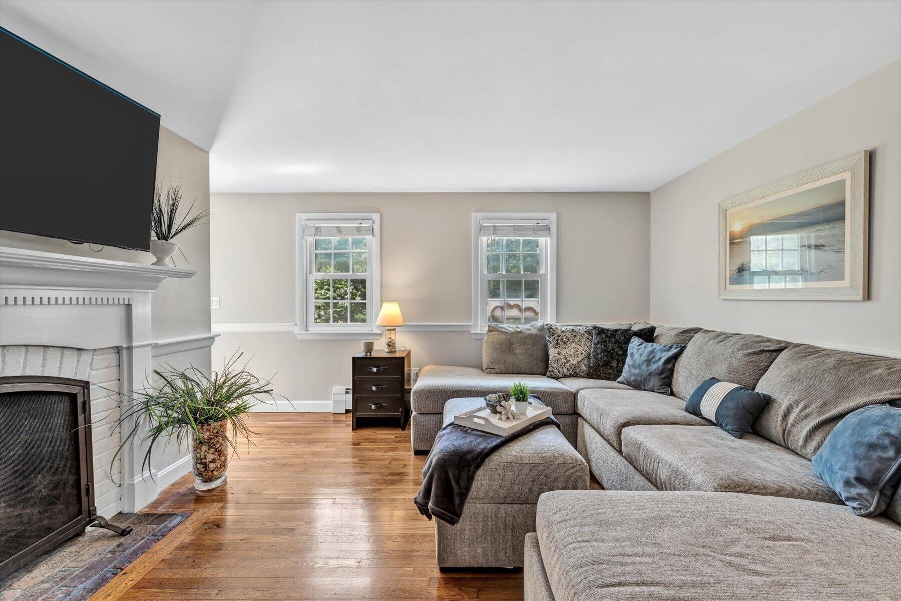Living room with a white fireplace, gray sectional sofa, and hardwood floors.