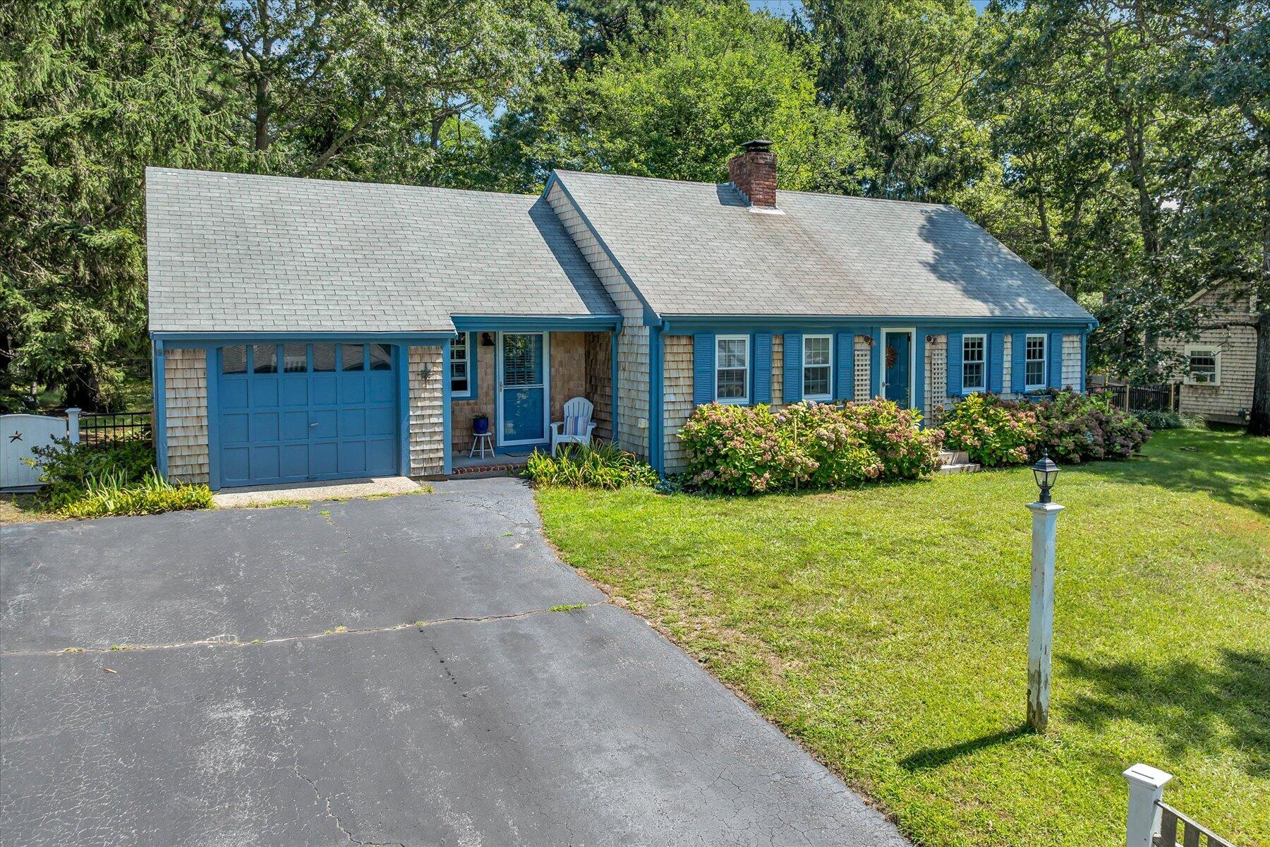 Shingle-sided home with blue trim, an attached garage, and flowering hydrangeas along the front.