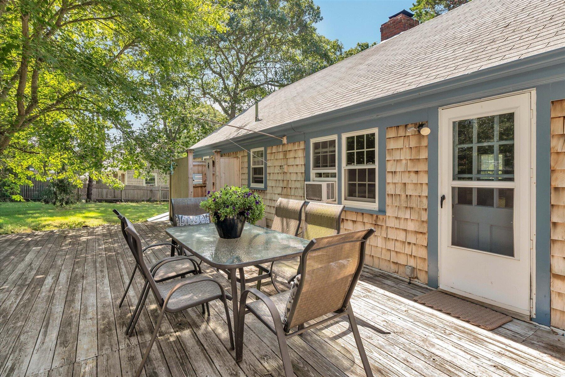 Wooden deck with outdoor dining set beside a shingle-sided home and leafy yard.