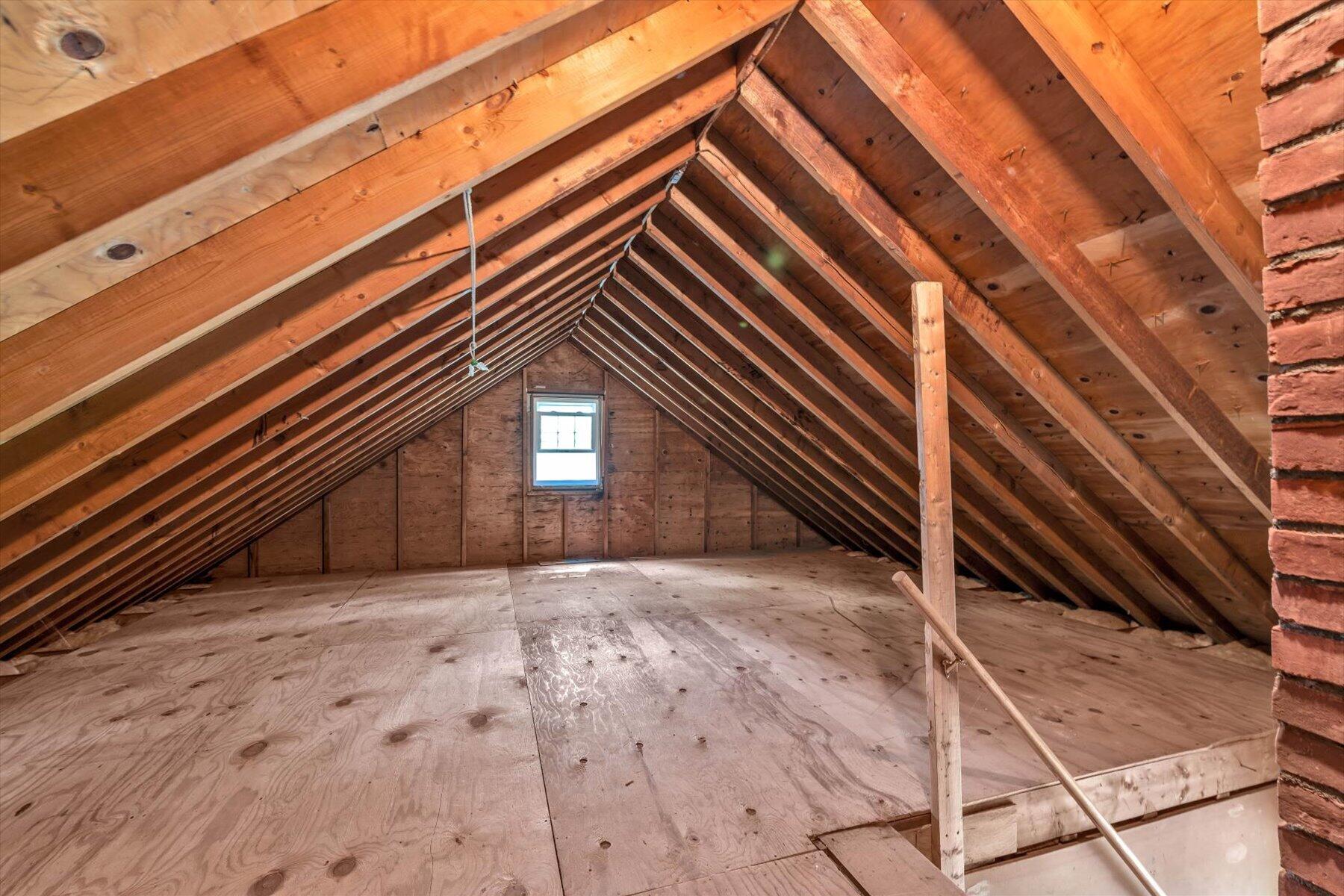 Unfinished attic with exposed roof rafters and a small end window
