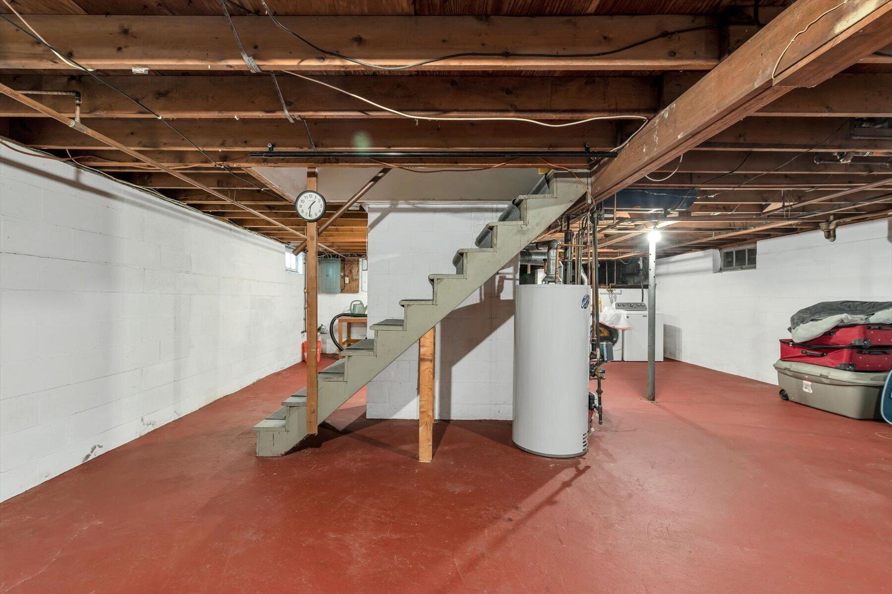Basement with exposed ceiling joists, a central staircase, and a water heater.