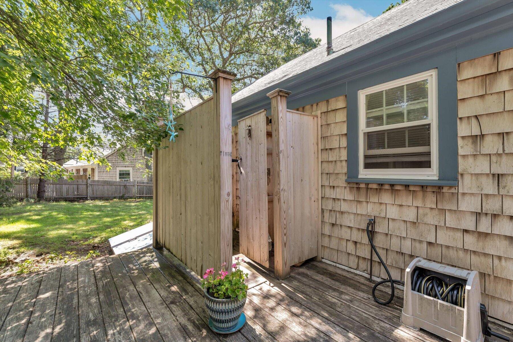 Outdoor shower beside a shingled home, with a weathered deck and fenced yard.
