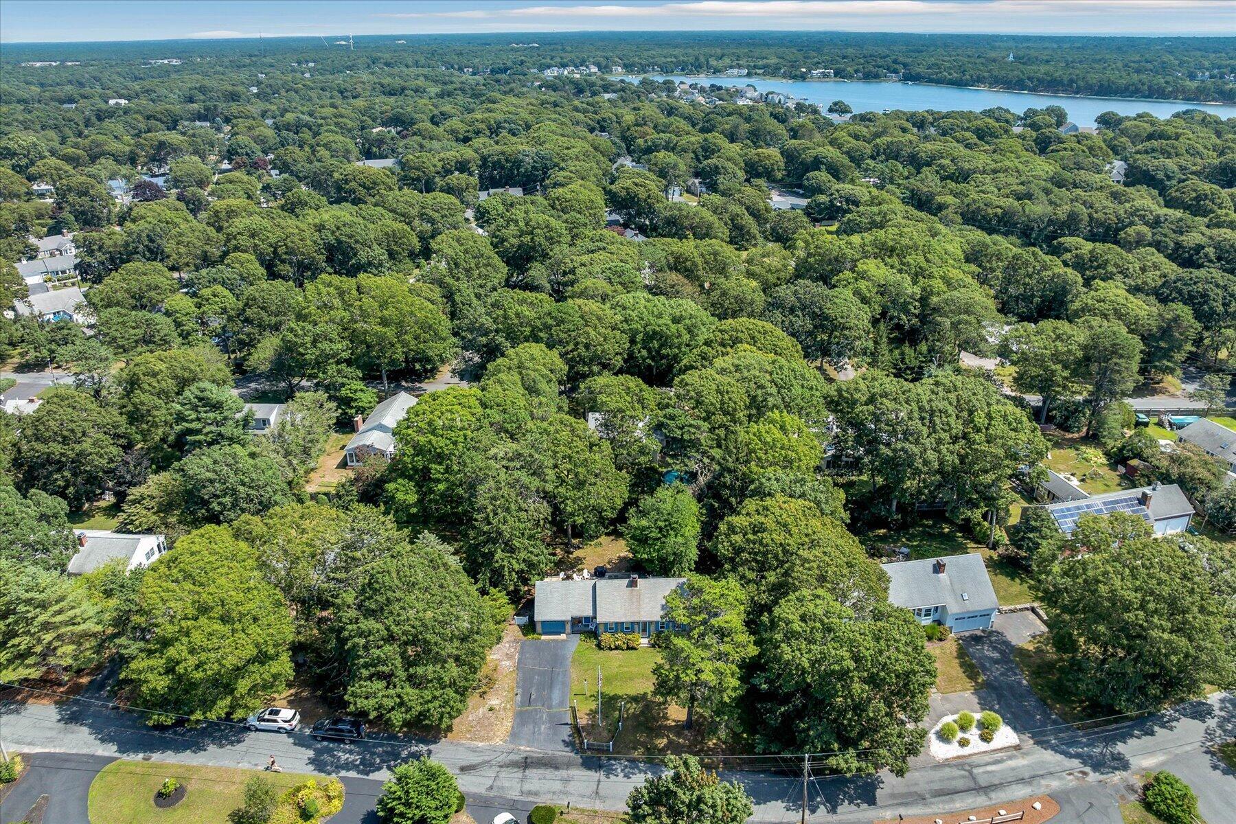 Aerial view of 20 Green Way amid tree-lined homes, with water visible in the distance.