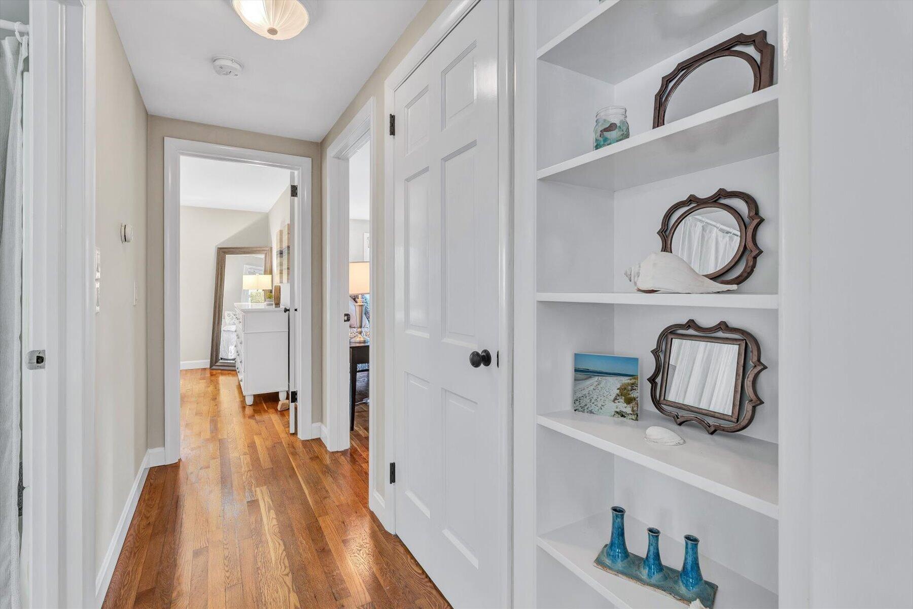 Hallway with hardwood floors, white doors, and built-in shelves displaying mirrors and coastal décor.