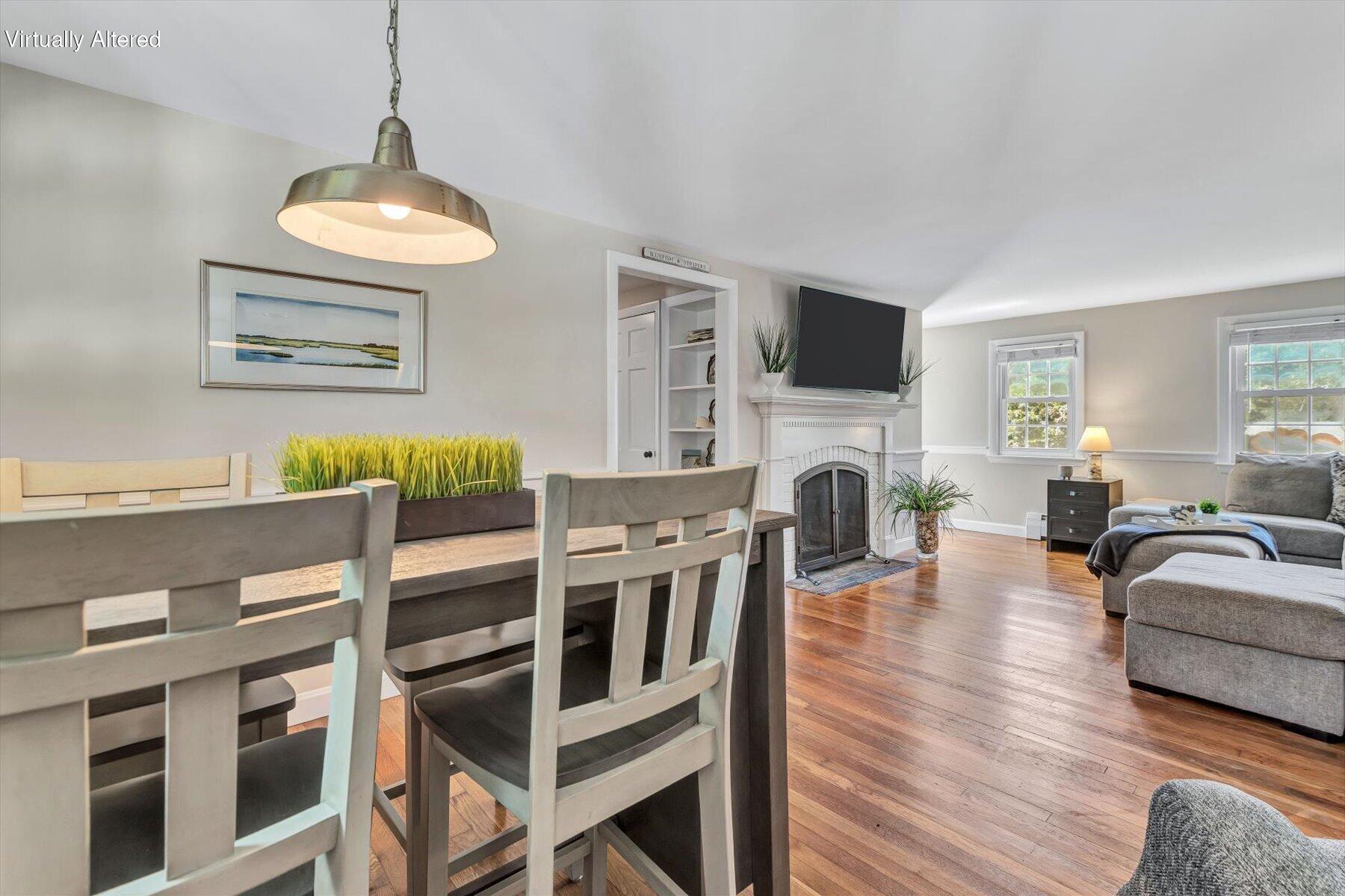 Open living and dining room with hardwood floors, a white fireplace, and gray seating.