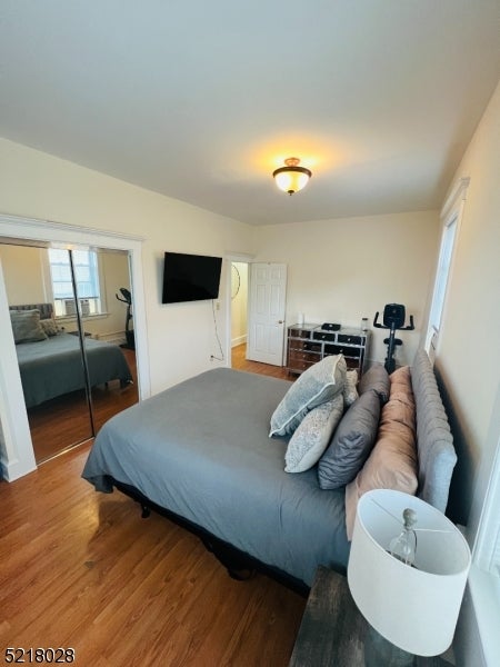 Bedroom with a gray bed, hardwood floors, mirrored closet doors, and a wall-mounted television.