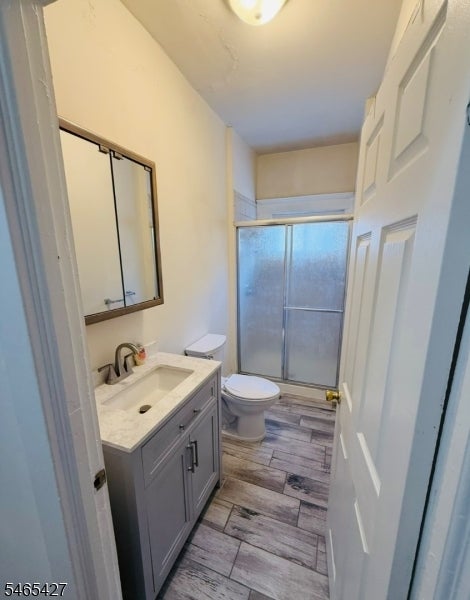 Bathroom with a gray vanity, toilet, frosted-glass shower, and gray wood-look tile floor.