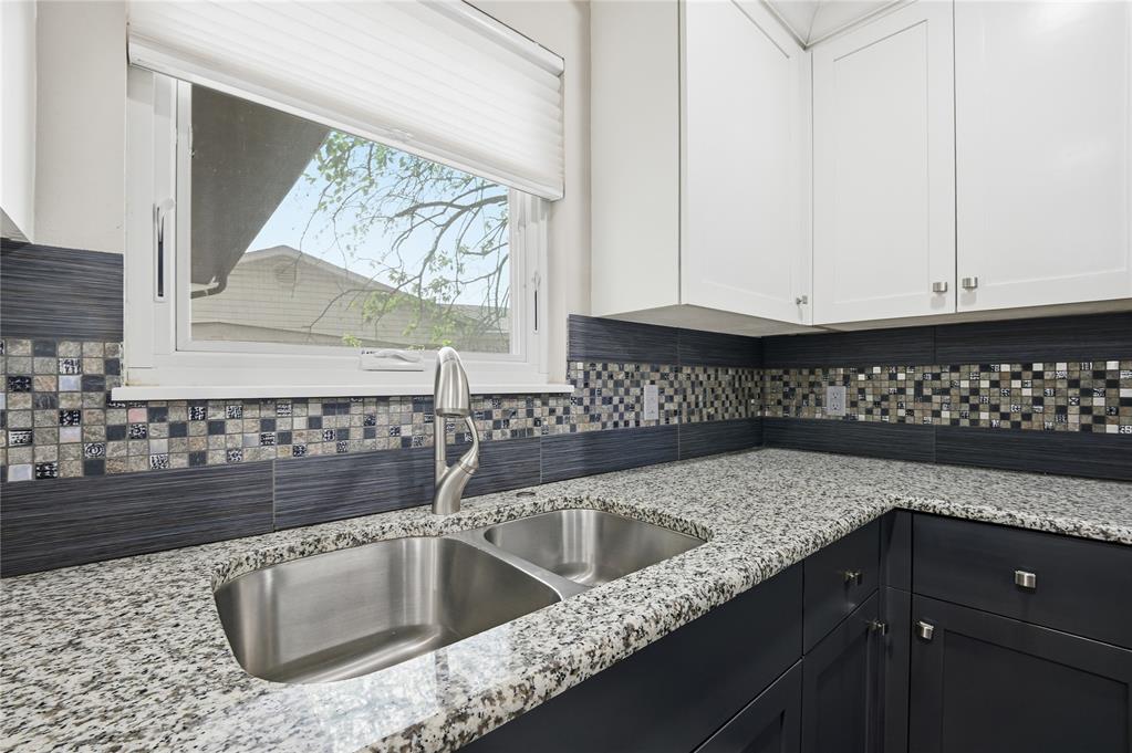 Kitchen with a stainless-steel double sink, speckled granite counters, and mosaic tile backsplash.
