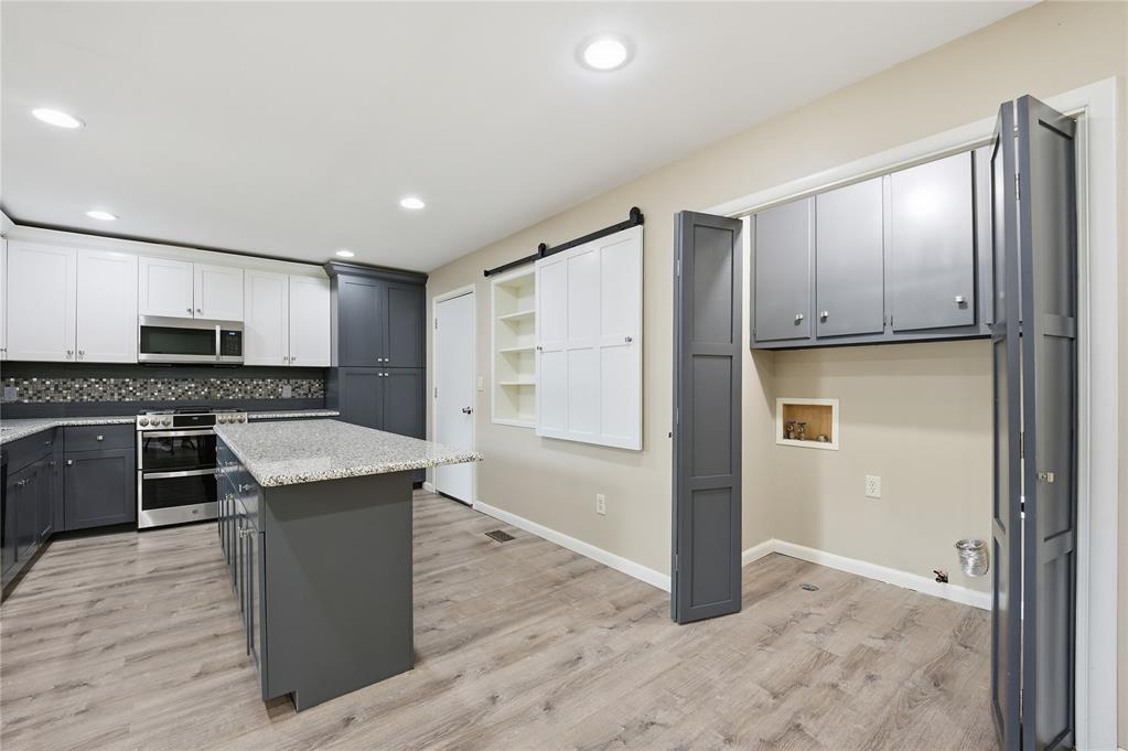 Kitchen with gray island, white cabinetry, stainless steel appliances, and light wood-look flooring.