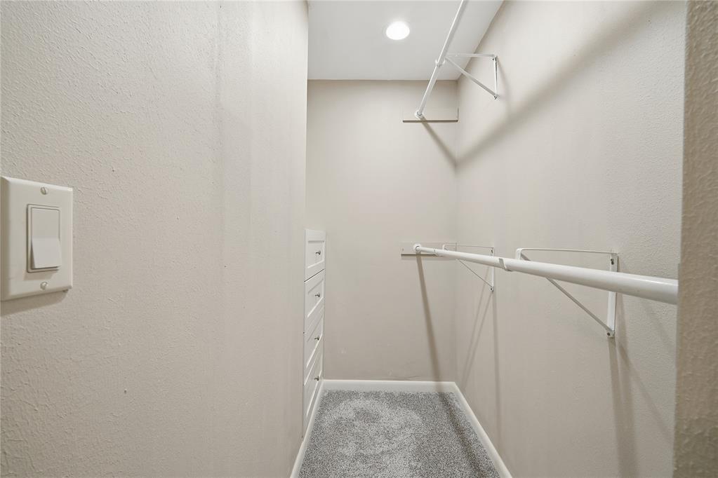 Walk-in closet with built-in drawers, gray carpet, and hanging rods.