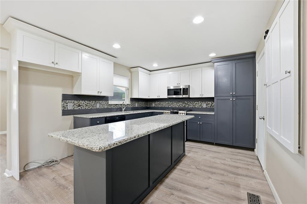 Kitchen with a large granite island, dark gray cabinets, and a mosaic tile backsplash.