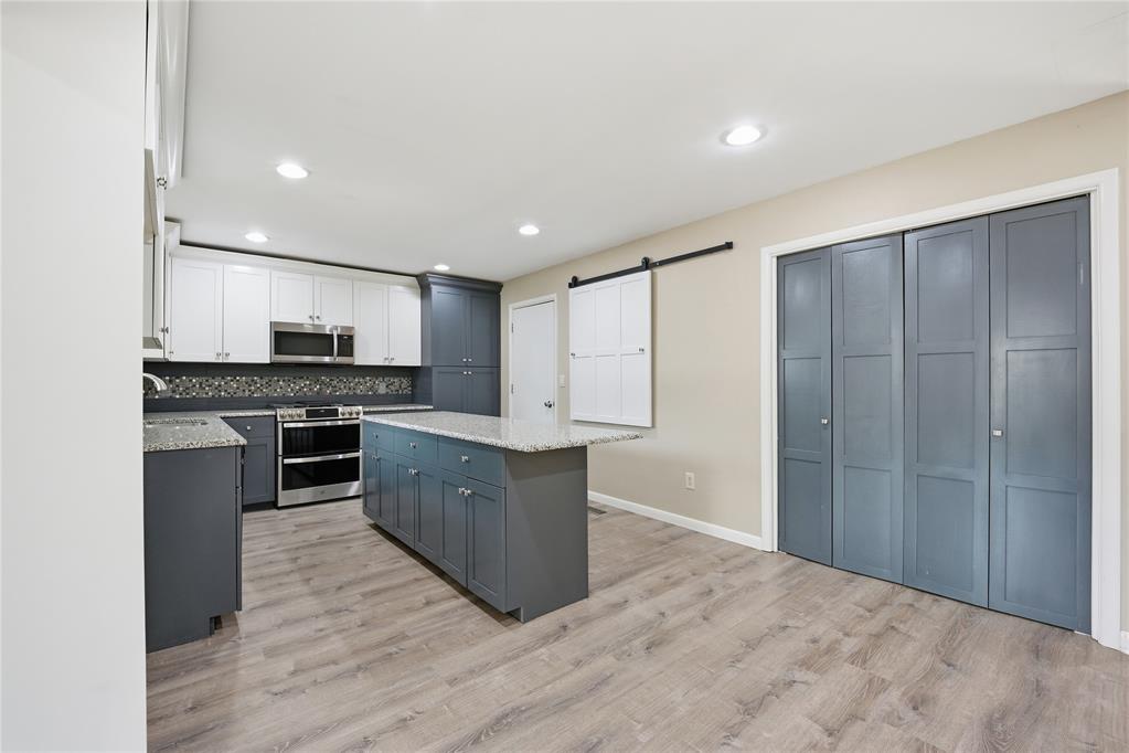 Kitchen with slate-blue cabinets, granite island, stainless steel appliances, and wood-look floors.