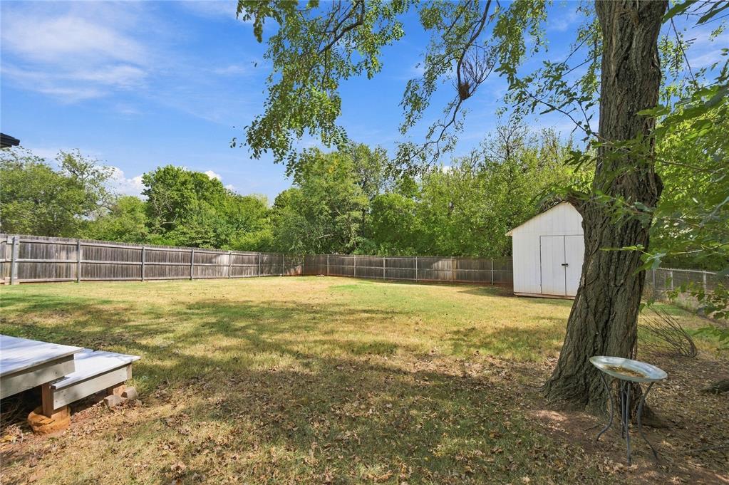 Fenced backyard with a white storage shed, broad lawn, and large shade tree.