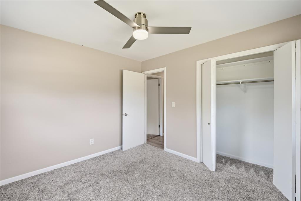 Empty bedroom with gray carpet, a ceiling fan, and an open closet.