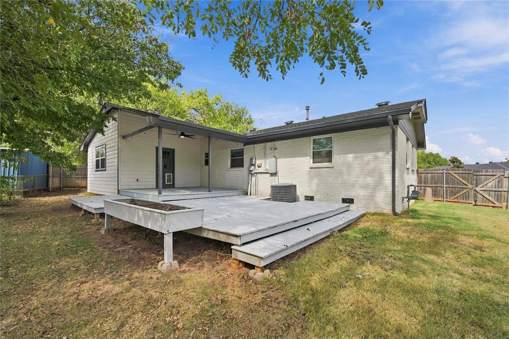 Rear of a light-colored house with a raised deck and covered patio in a fenced backyard.