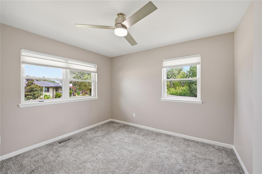 Empty bedroom with gray carpet, two windows with white blinds, and a ceiling fan.
