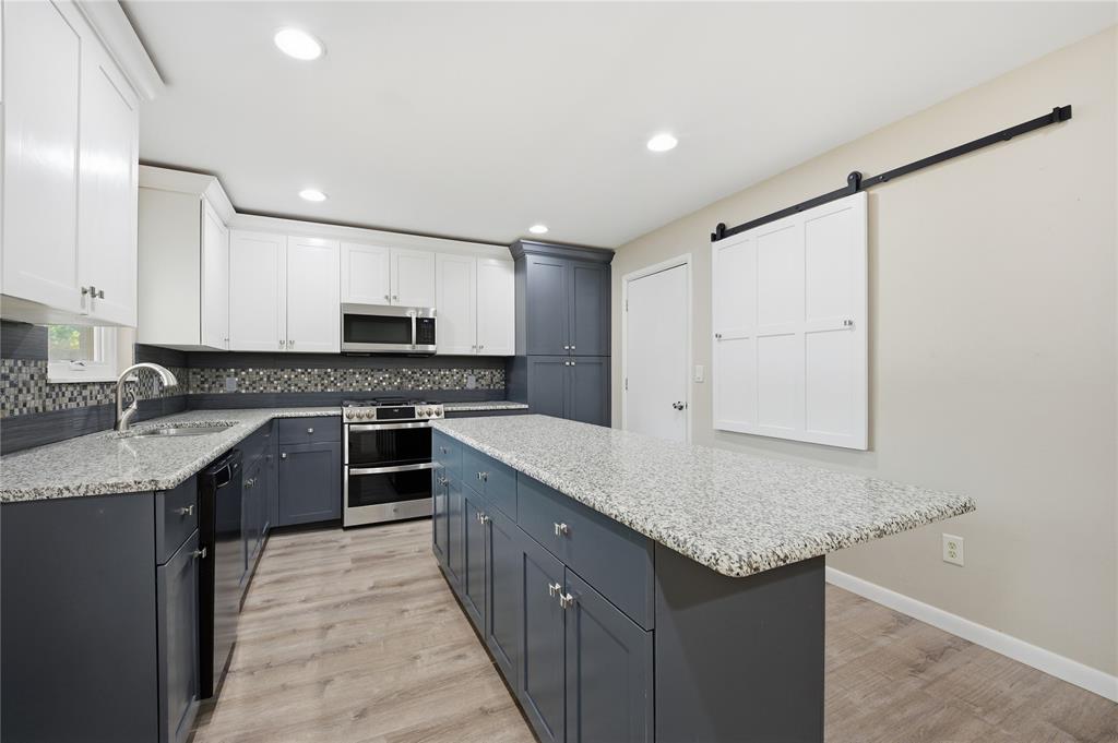 Kitchen with blue-gray cabinets, granite peninsula, stainless steel appliances, and a mosaic tile backsplash.