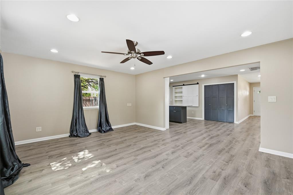 Vacant living room with gray plank flooring, ceiling fan, and an opening to the kitchen.