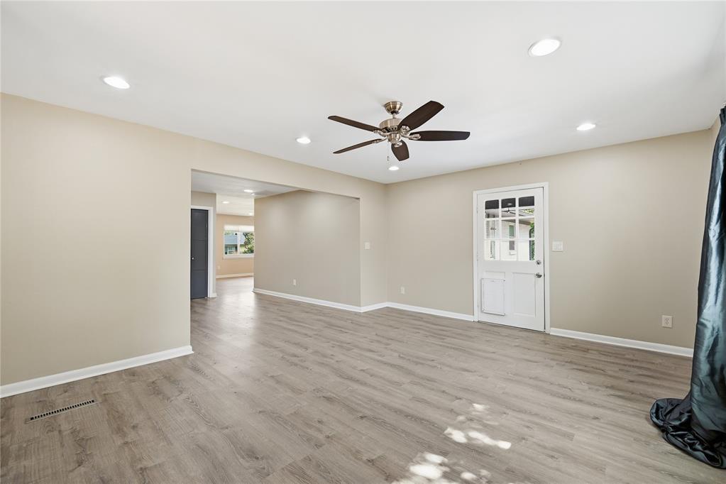 Empty living room with gray wood-look flooring, a ceiling fan, and a glass-panel door.